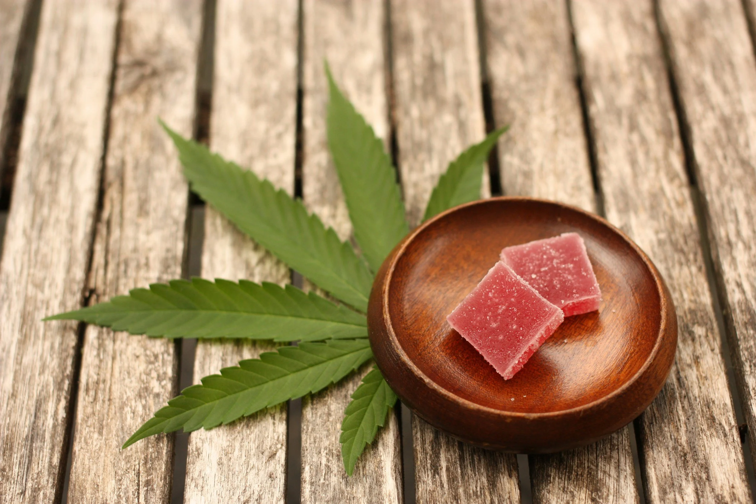 Close-up of pink cannabis products in a wooden bowl with fresh cannabis leaves.