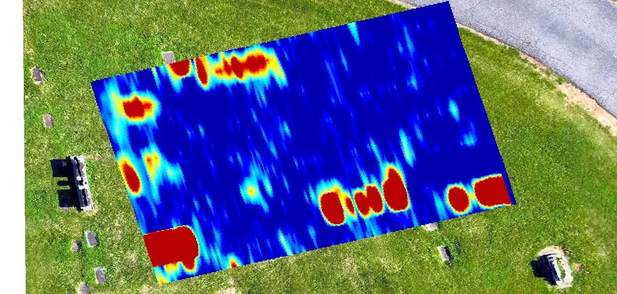 A heatmap overlay on a grassy park area showing heat distribution, with red indicating high activity and blue low activity, adjacent to a paved road and benches.