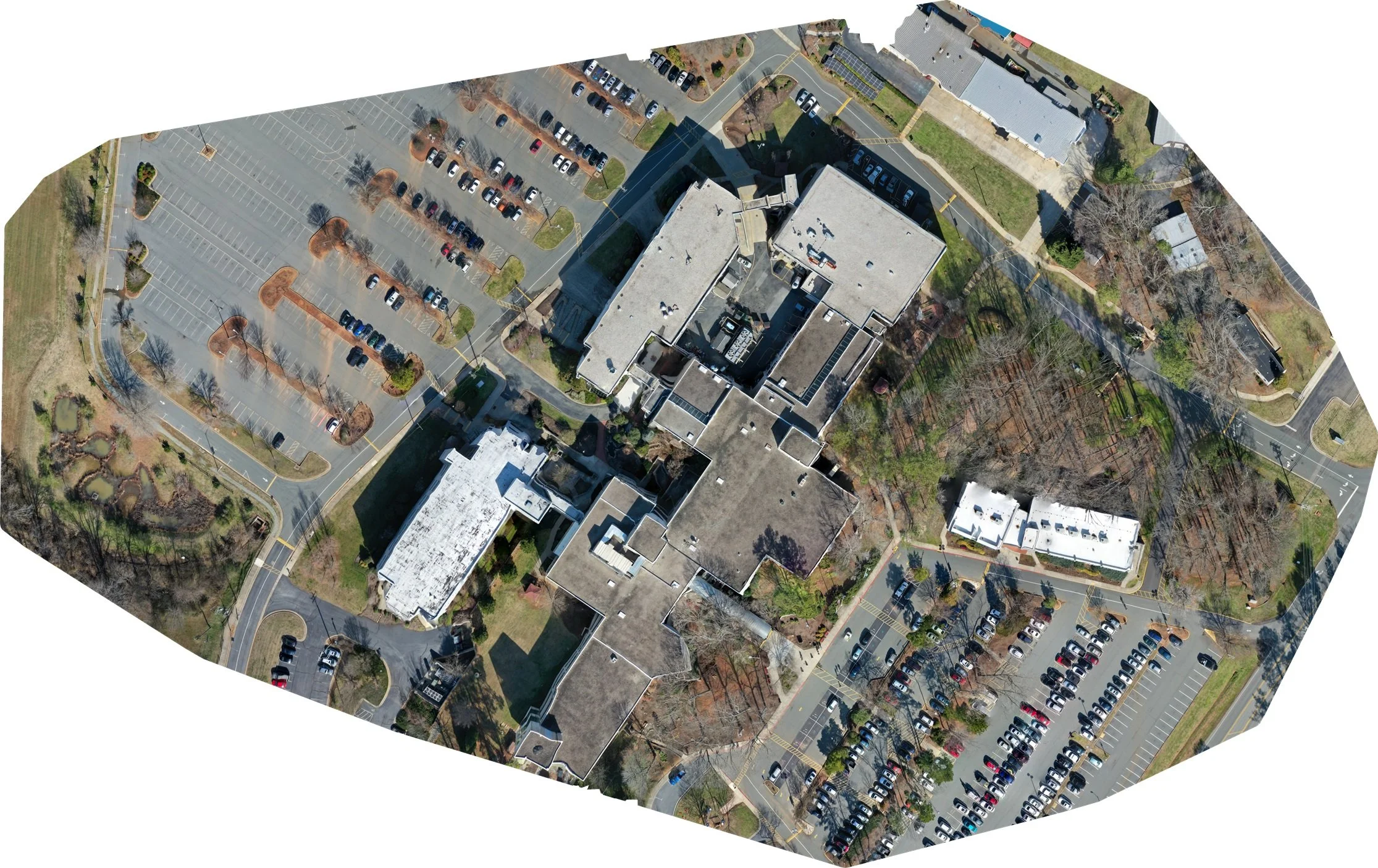 Aerial view of a parking lot and surrounding buildings, with trees and roads, taken from high above on a clear day.