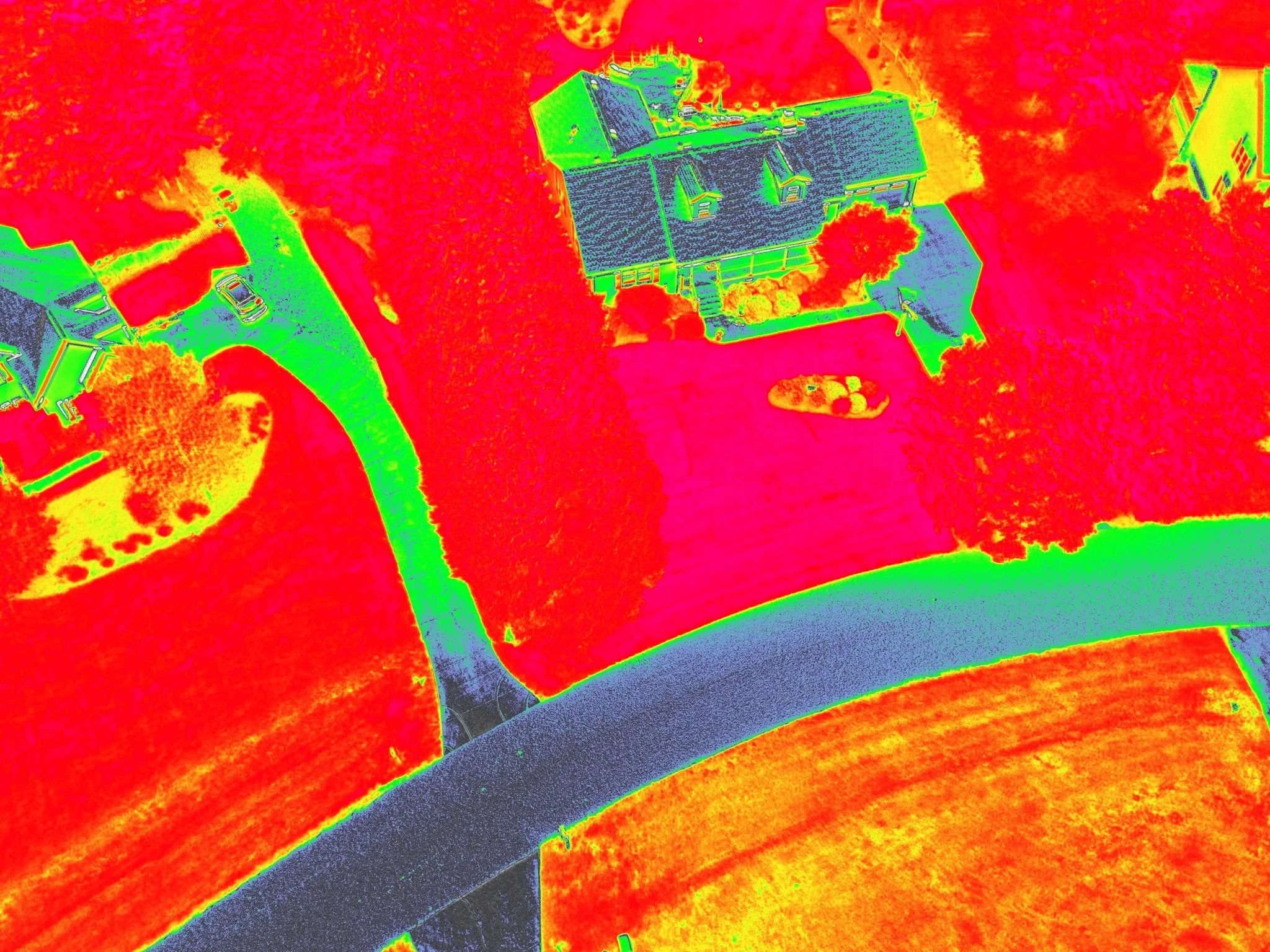 Infrared thermal image of a house and surrounding yard, showing different temperatures with colors ranging from red to green and blue.
