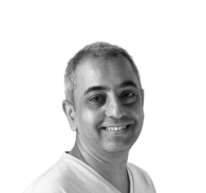 Smiling man with short hair wearing a light-colored shirt, photographed against a dark background.