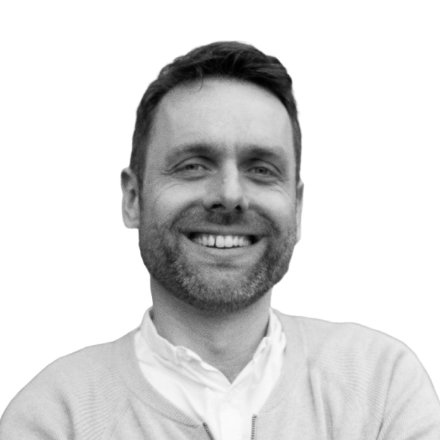 A smiling man with short dark hair and a beard, wearing a light-colored jacket over a button-up shirt, against a plain white background.
