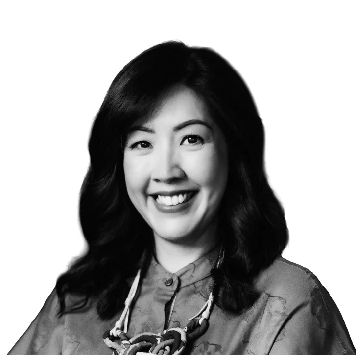 Black and white portrait of a smiling woman with dark wavy hair, wearing a patterned top and a statement necklace.