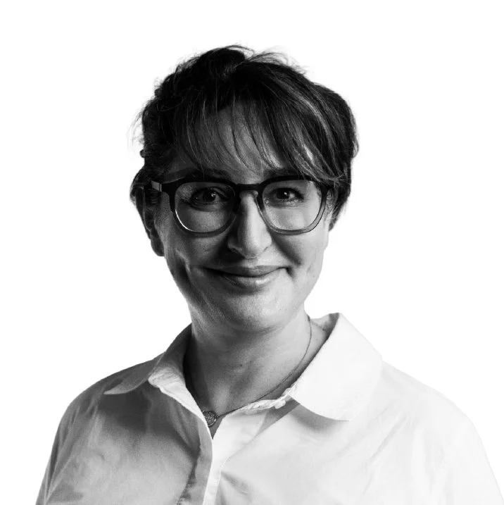 Black and white portrait of a woman with short hair and glasses, smiling, wearing a white collared shirt.