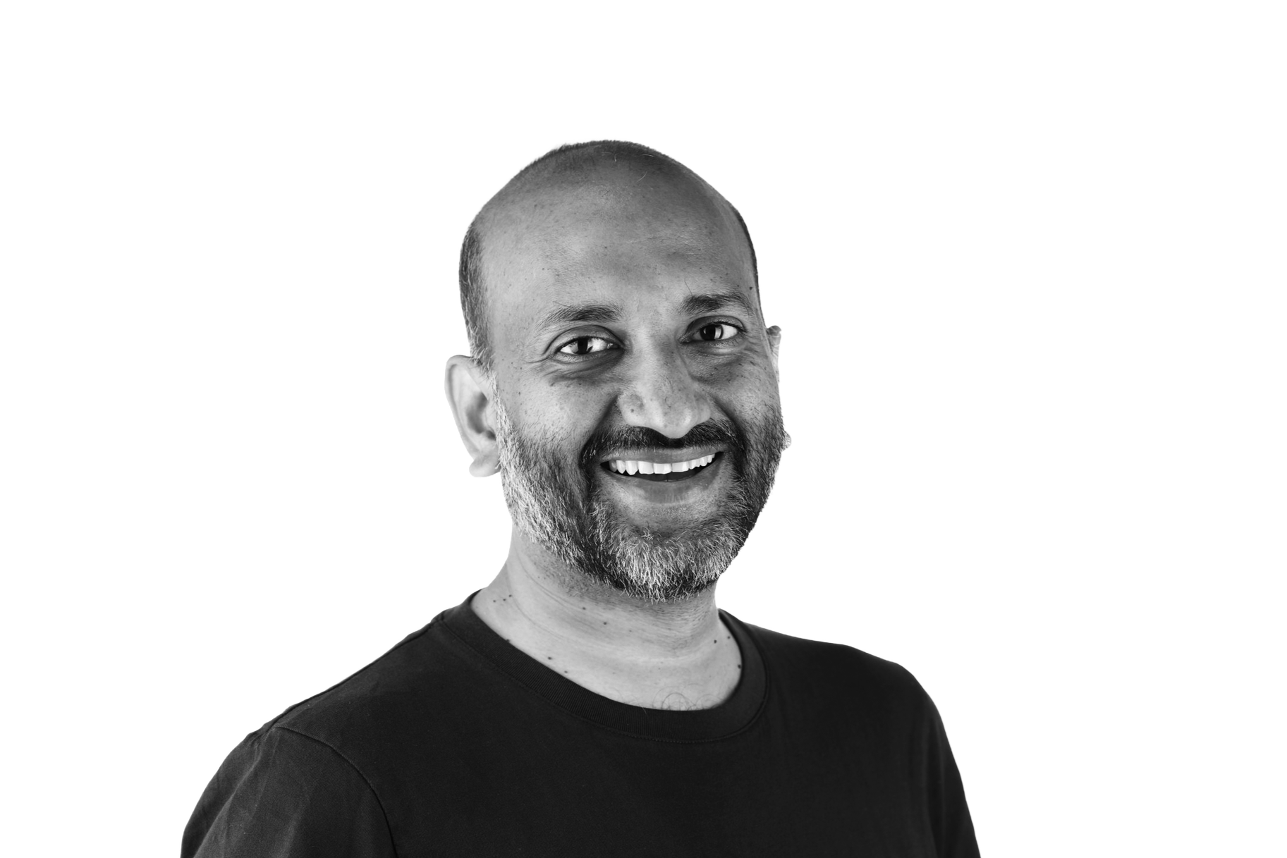 Black and white portrait of a smiling middle-aged man with a beard, wearing a dark t-shirt.