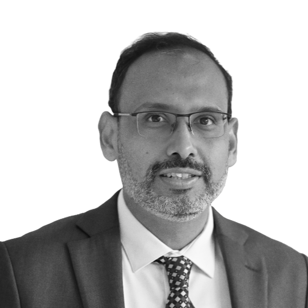 Black and white portrait of a man wearing glasses, a suit jacket, a white shirt, and a patterned tie, looking at the camera.