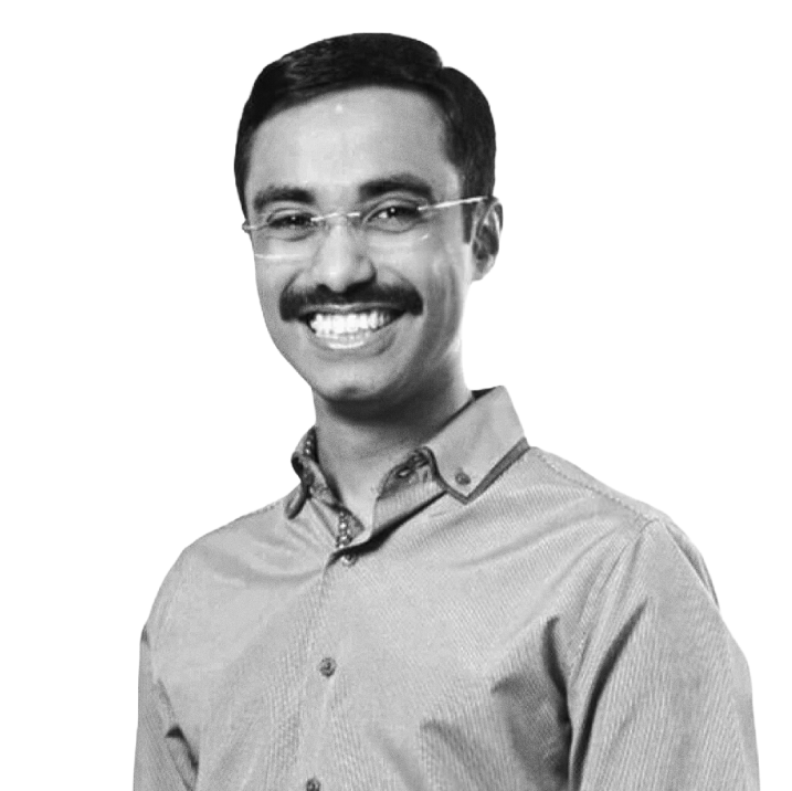 A smiling man with glasses and a mustache, wearing a collared shirt, in black and white