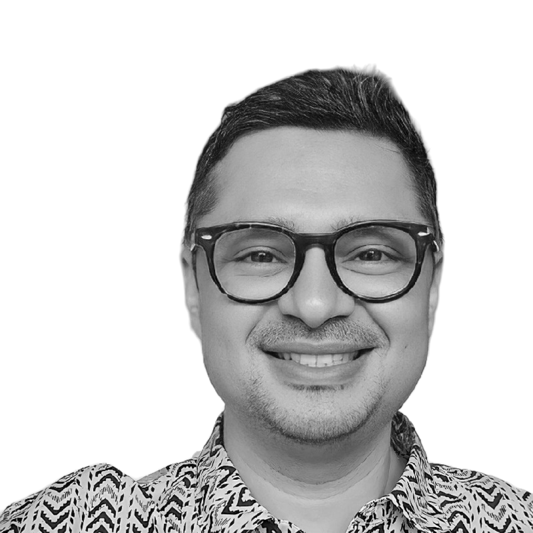 Black and white portrait of a smiling man with glasses, short dark hair, and a patterned shirt.