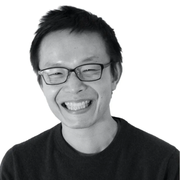 A smiling man with glasses and short dark hair, wearing a dark shirt, against a plain white background.