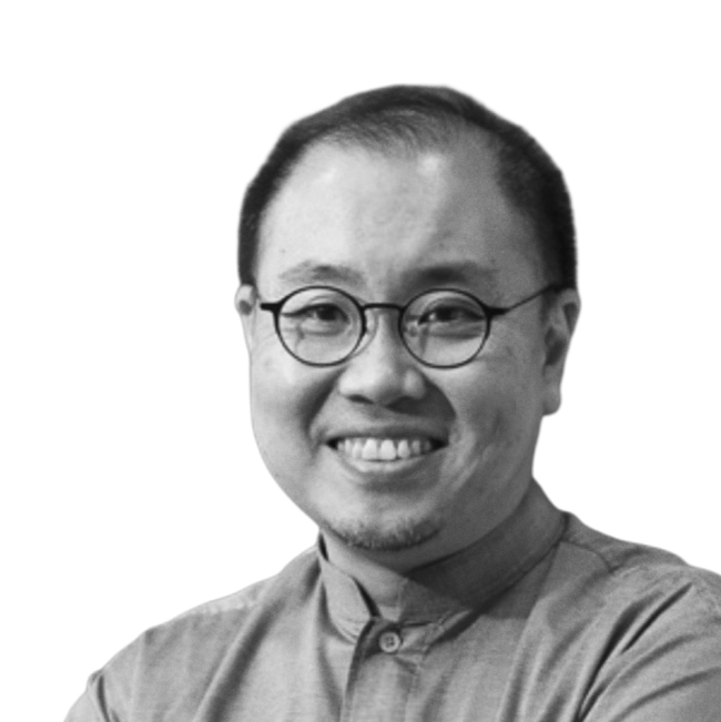 Black and white photo of smiling man with glasses, wearing a buttoned shirt.