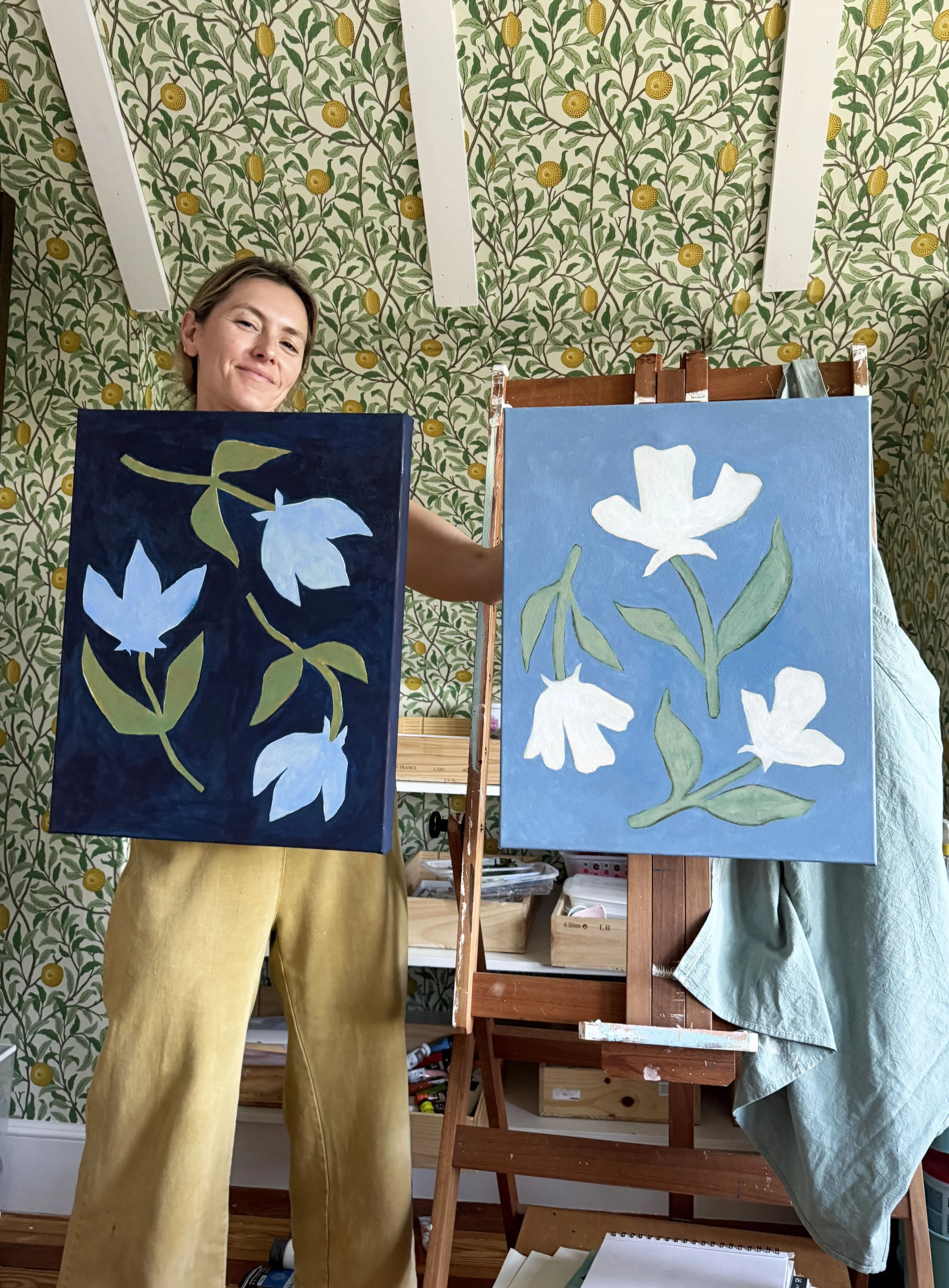 artist cris villa smiling while holding two paintings in her studio
