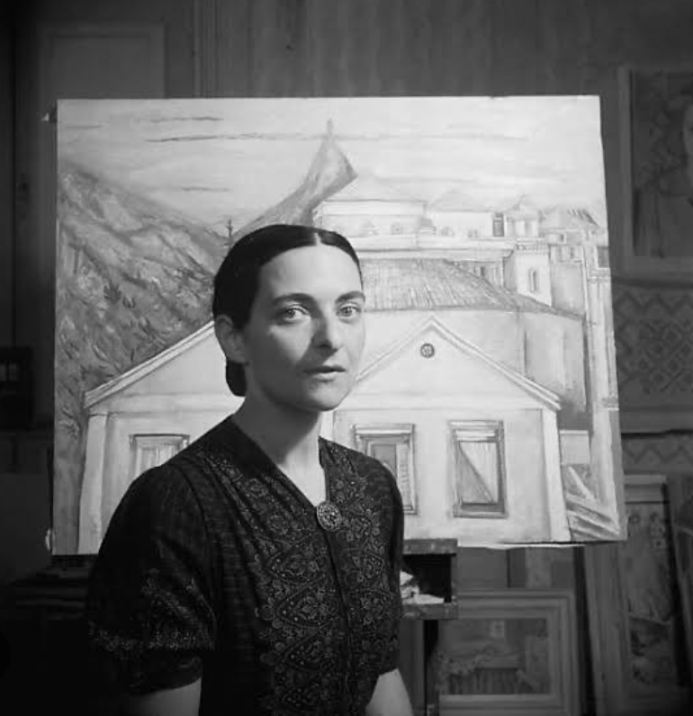 Female artist Maria Helena Vieira posing for the camera sitting in front of one of her paintings in a black and white picture