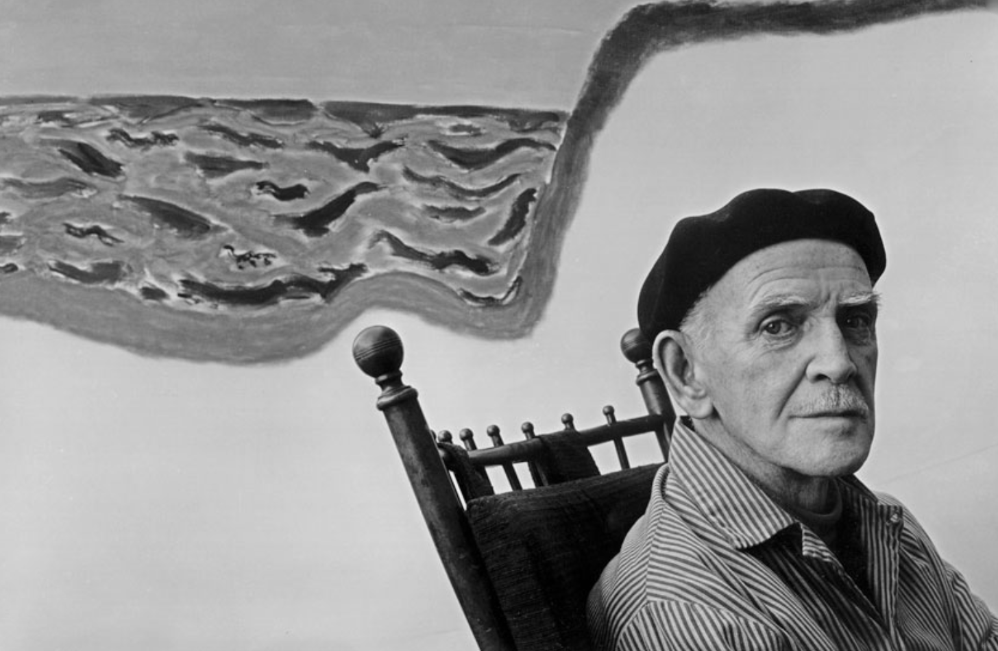 Picture portrait of Artist Milton Avery sitting on a chair in front of one of his paintings.