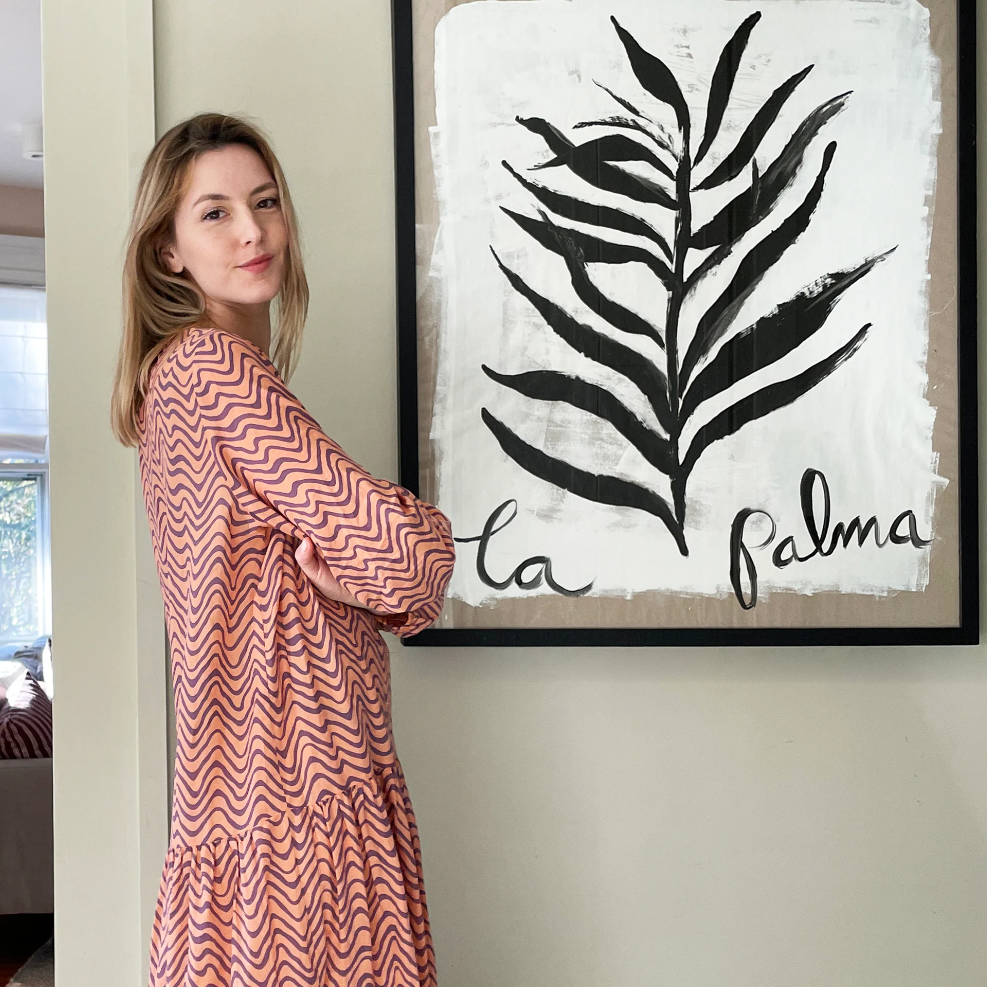 blonde female artist posing sideways in front of a large leaf painting with the words "la palma" in it