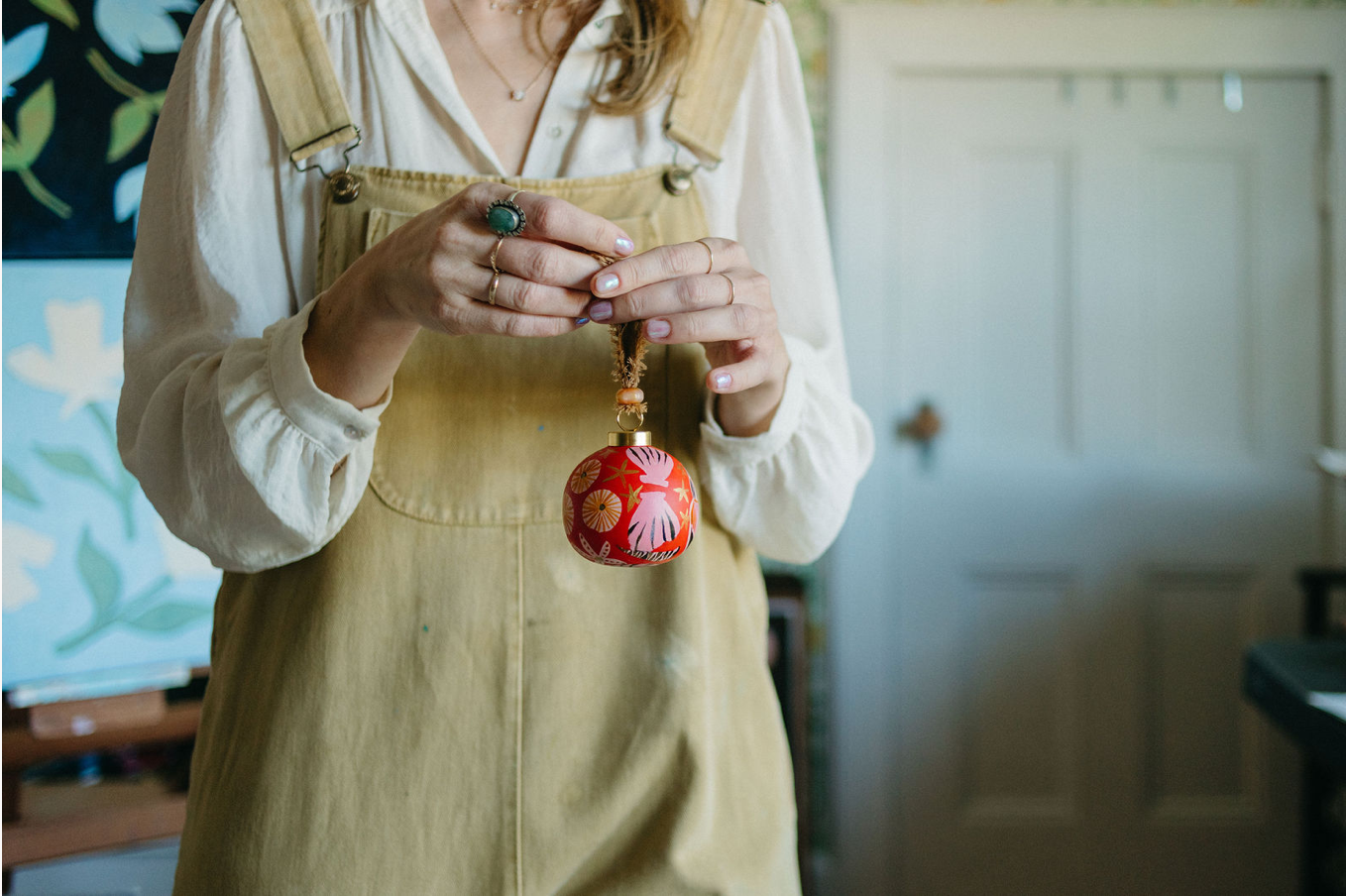artist cris villa holding a red ornament with seashell motifs