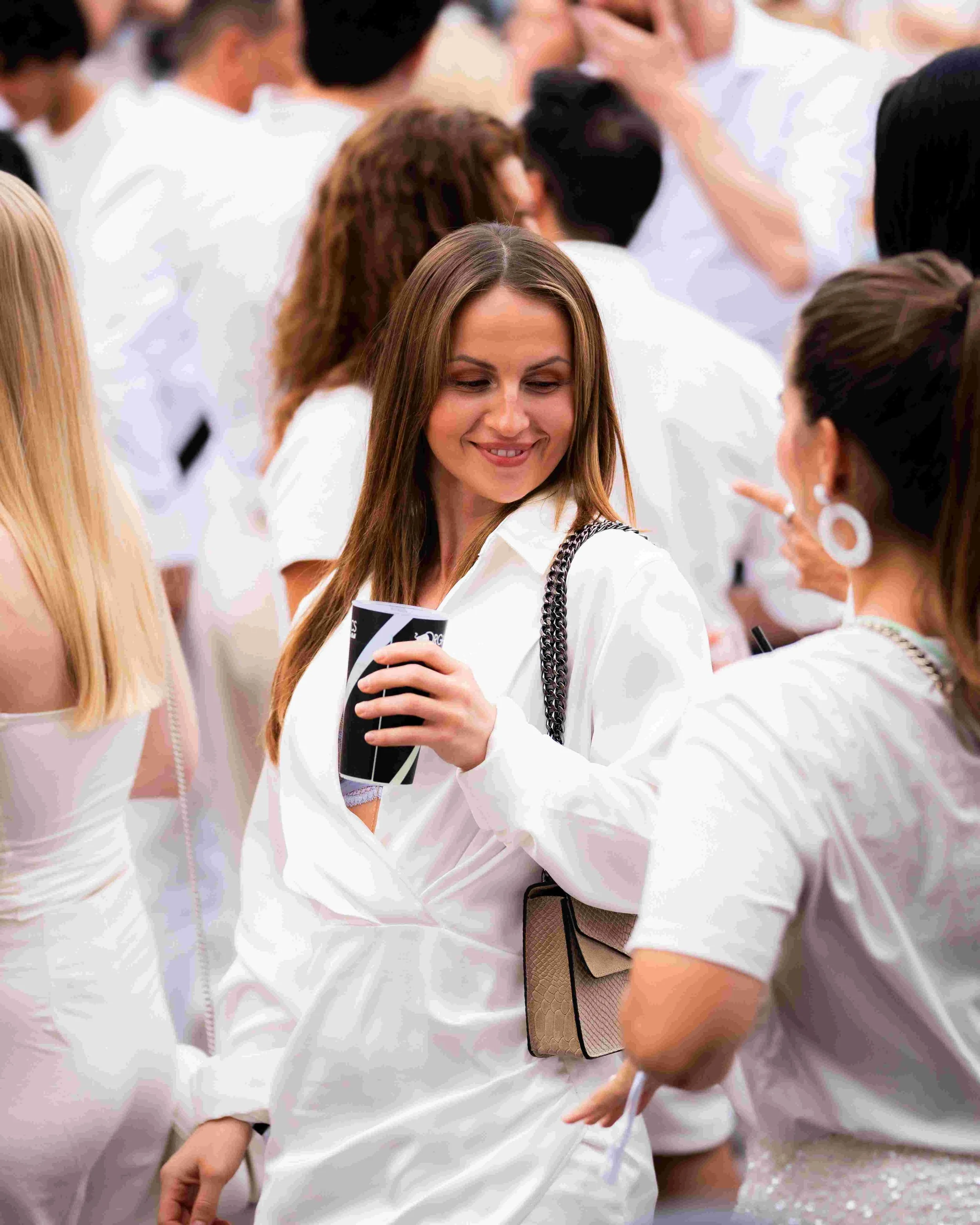 A group of women dressed in white, gathered closely together at an event, smiling and engaging in conversation.