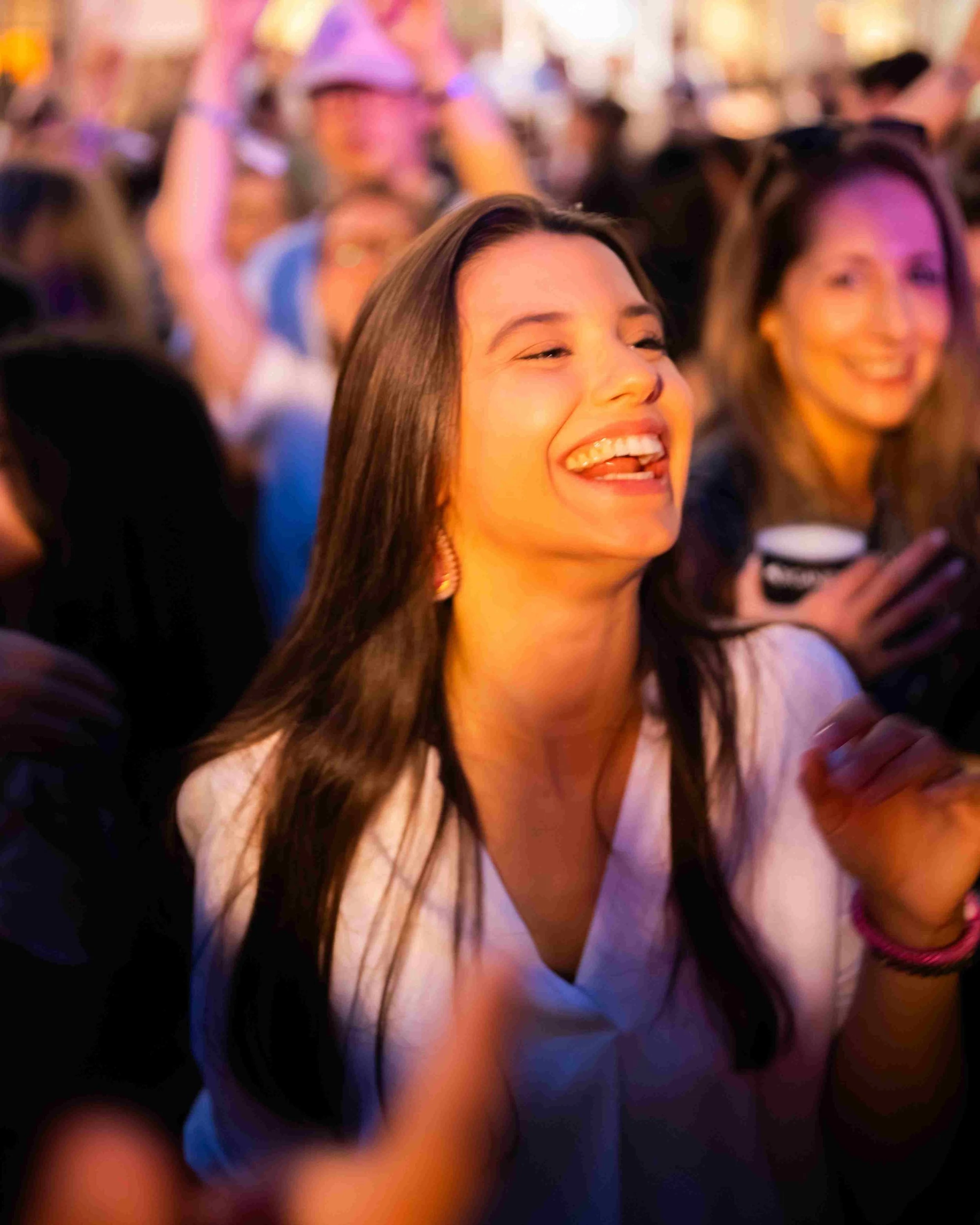 A group of young women at a lively social gathering, smiling and enjoying themselves, one woman in the foreground is singing or laughing.