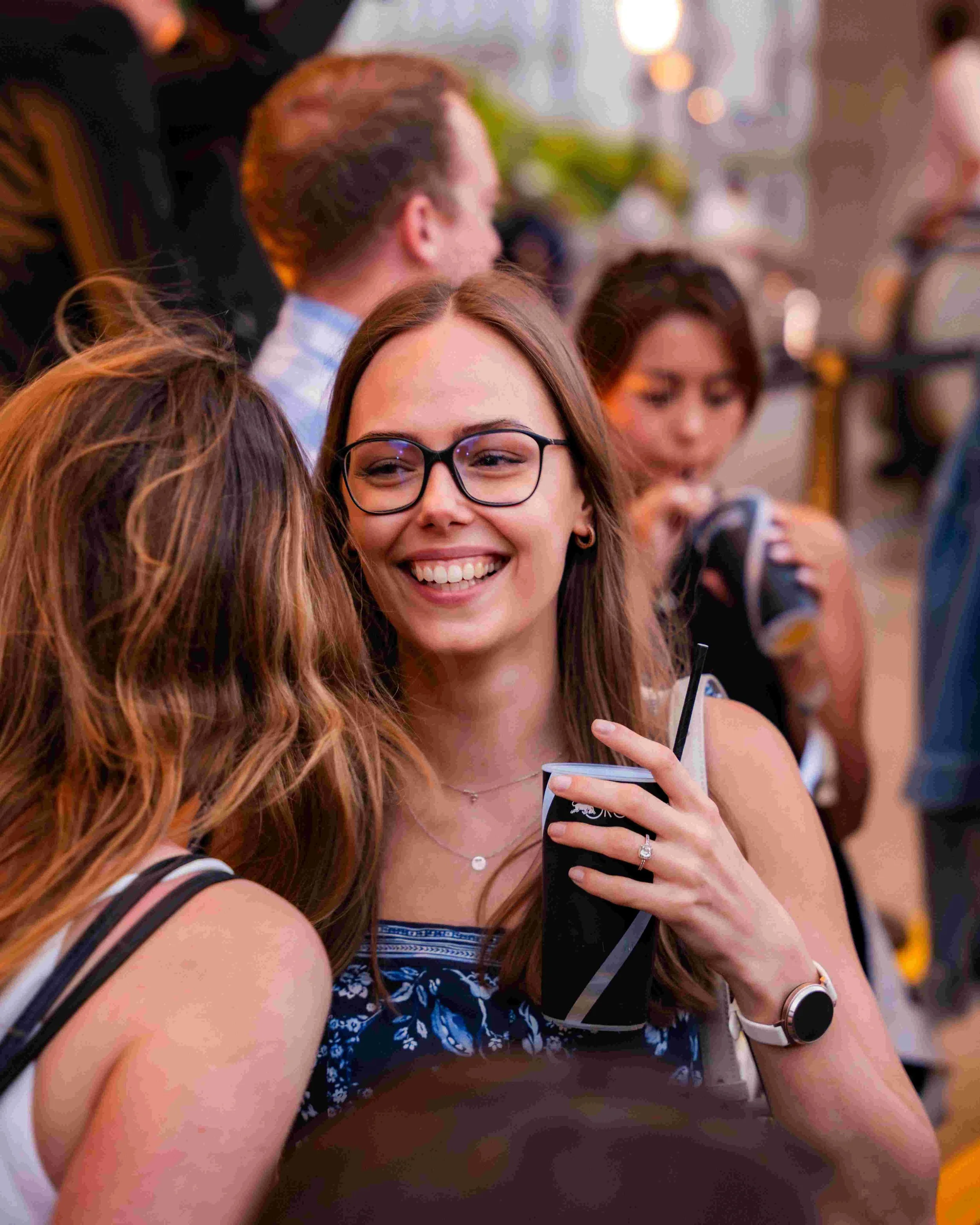 A group of women socializing at an indoor gathering, with some holding drinks and wearing casual summer attire.
