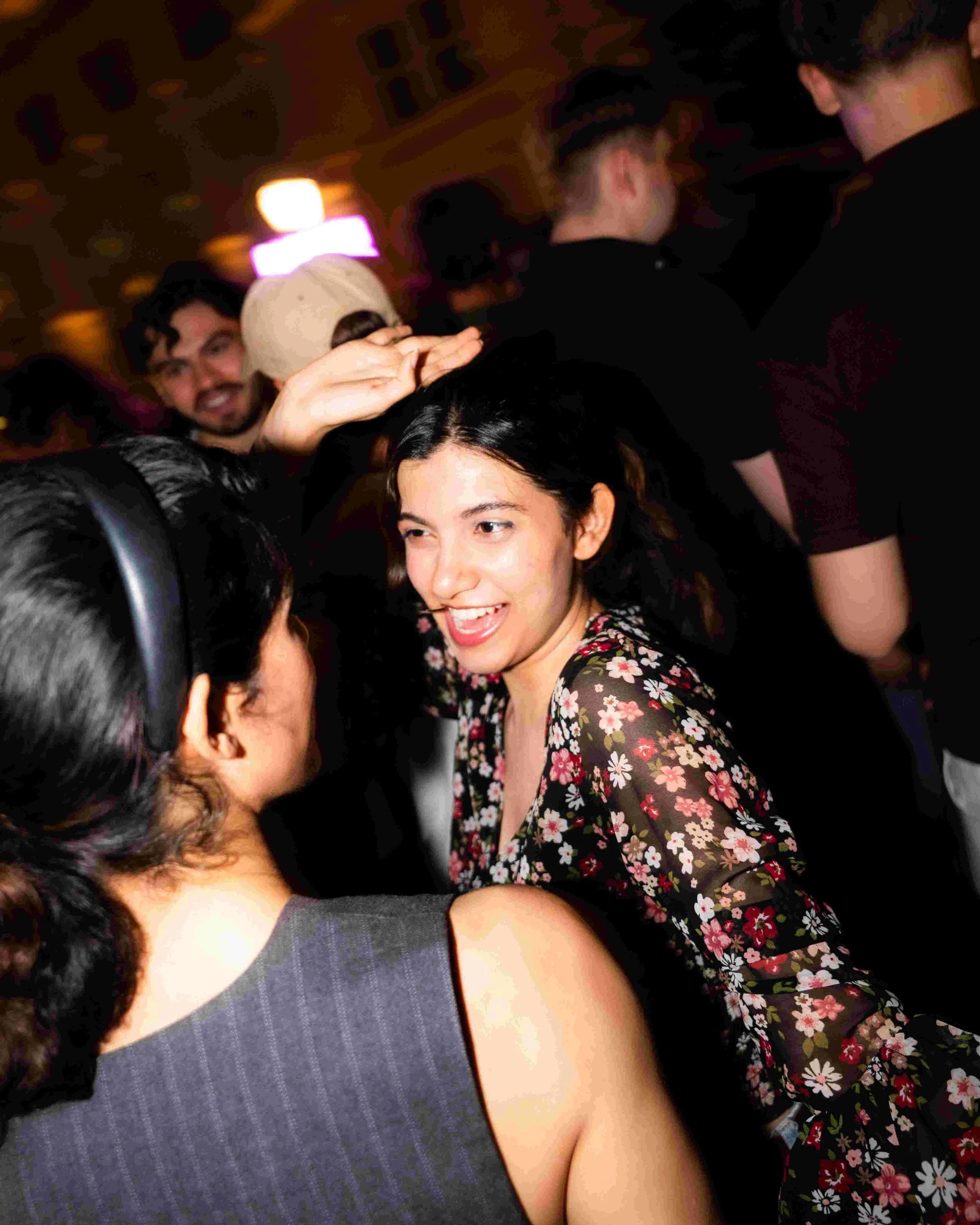 People hugging and smiling in a crowded indoor setting with warm lighting.