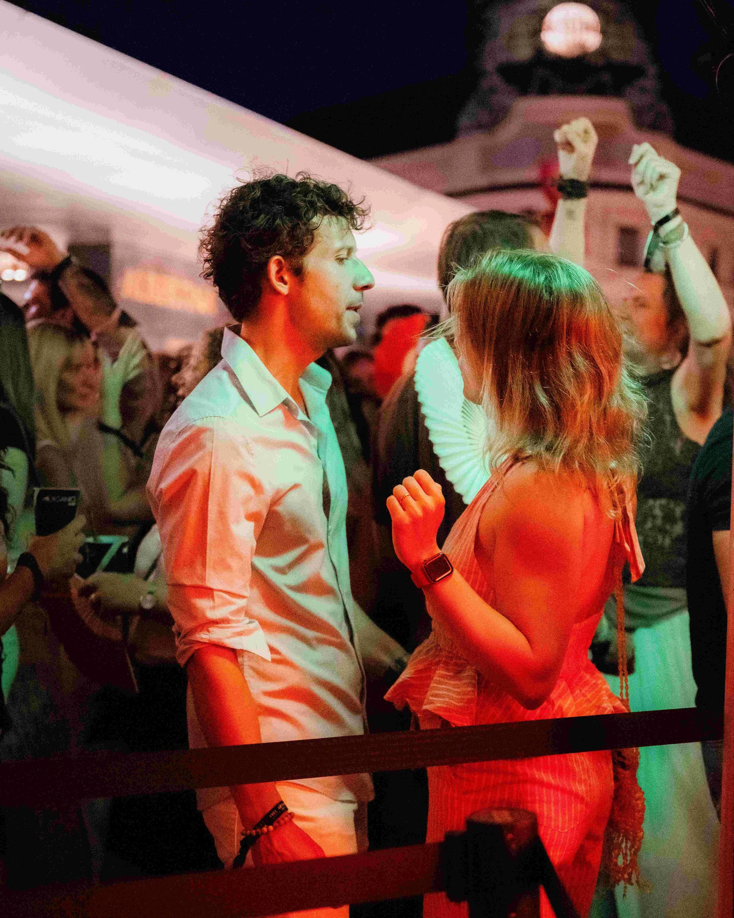A group of people dancing and socializing at a party or nightclub, with colorful lighting and a relaxed atmosphere.