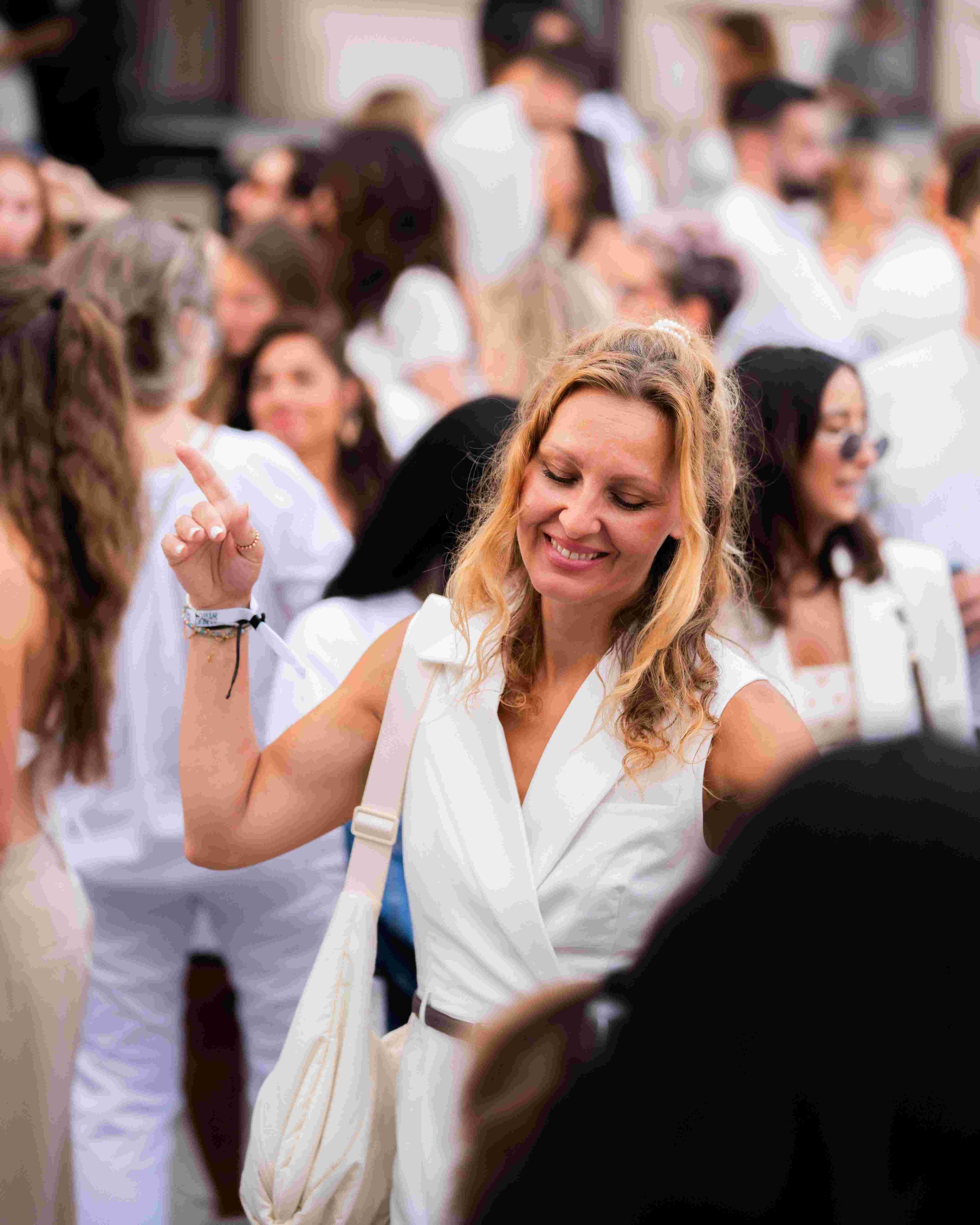 A group of people at a wedding, with a woman in focus smiling and dancing among others dressed in white and other colors.