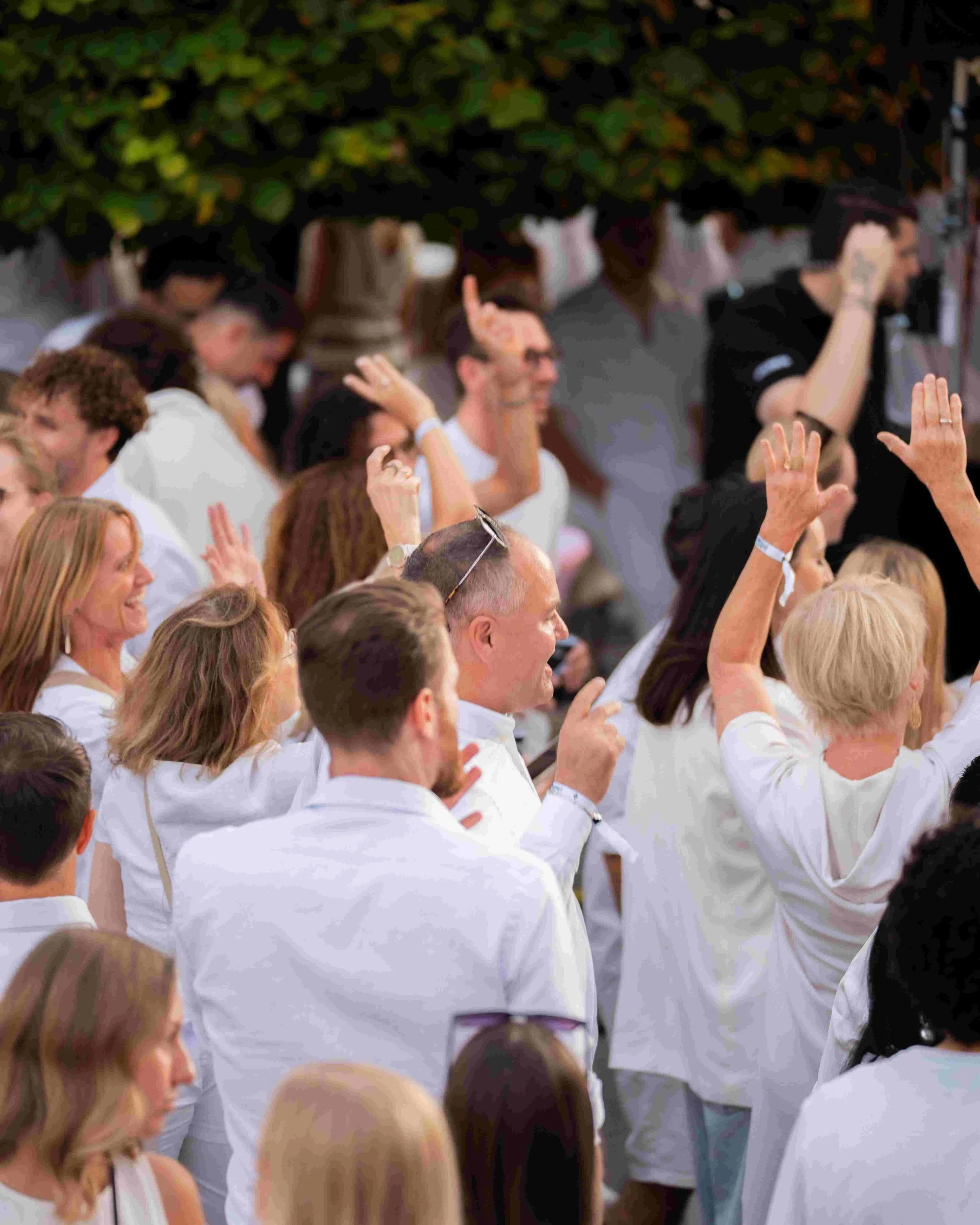 Crowd of people wearing white shirts at a gathering, with some raising their hands.