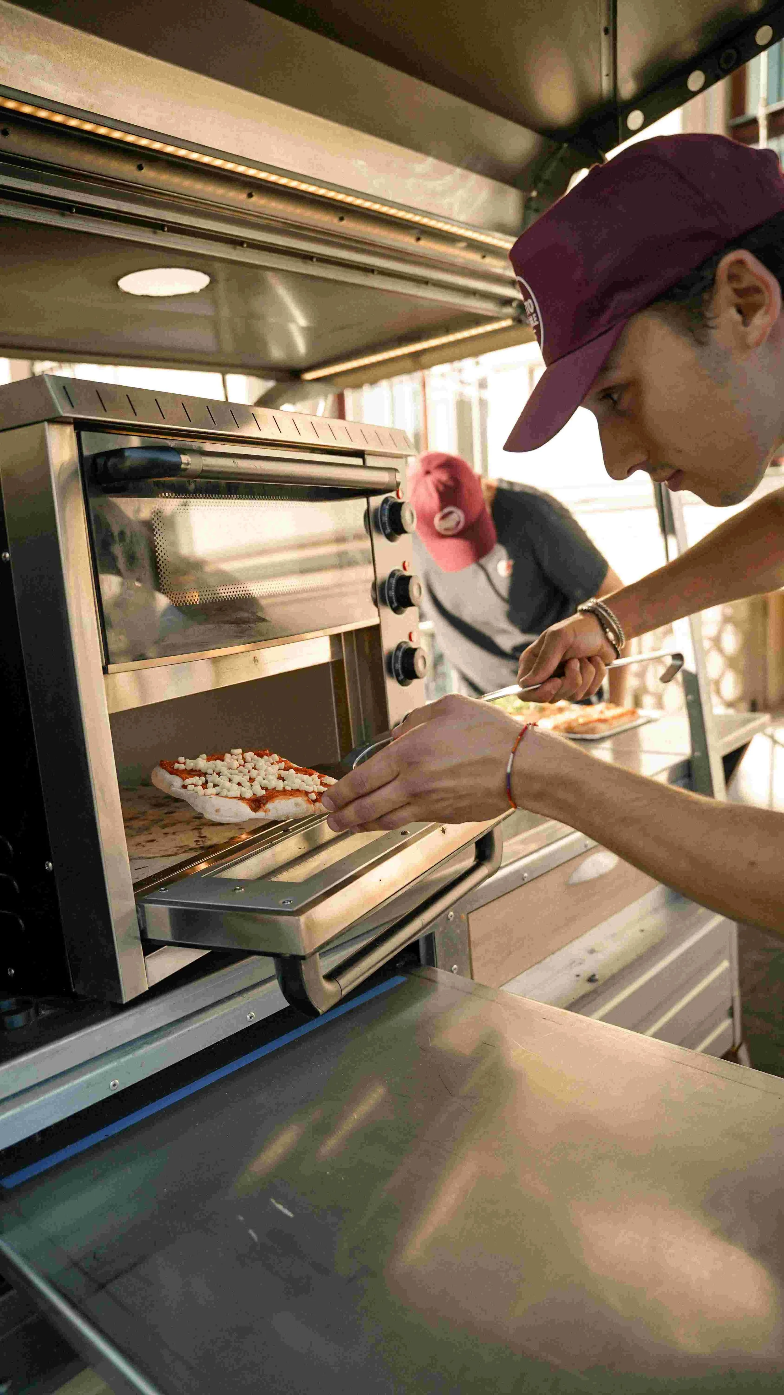 Person placing pizza in a commercial pizza oven at a pizzeria