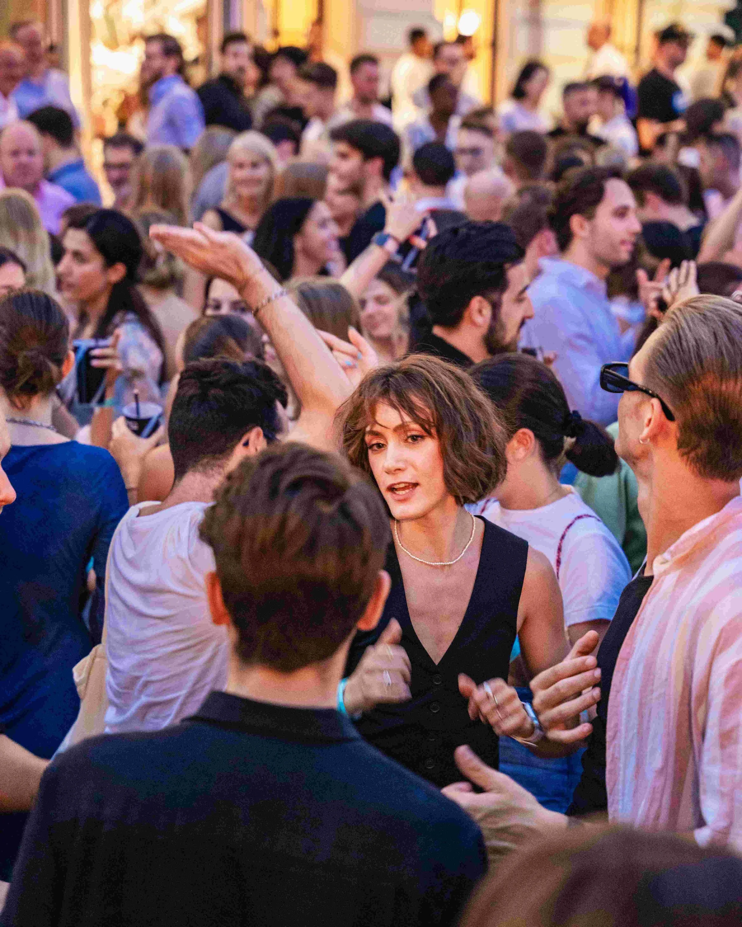 People dancing and socializing at a lively indoor party or celebration, with warm lighting and elegant decor.