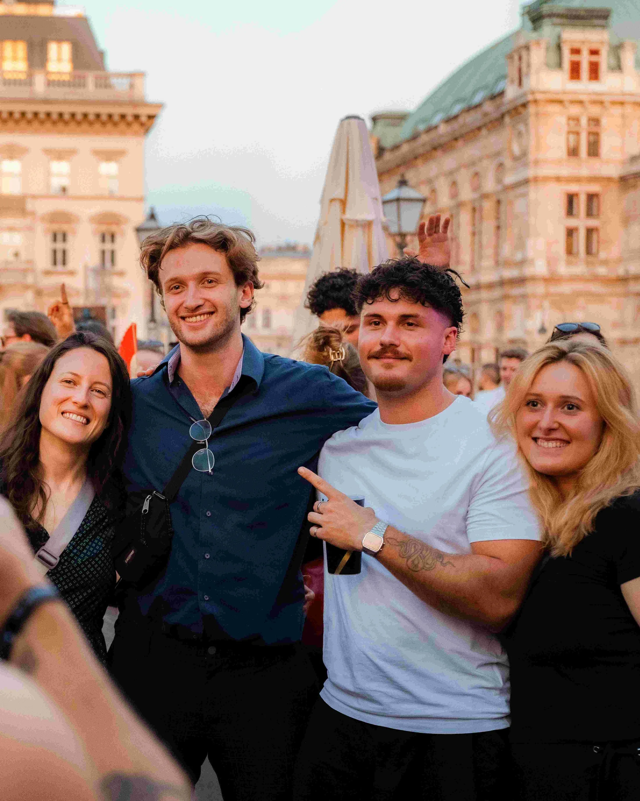 Group of smiling people gathered outdoors with historic buildings in the background during evening.