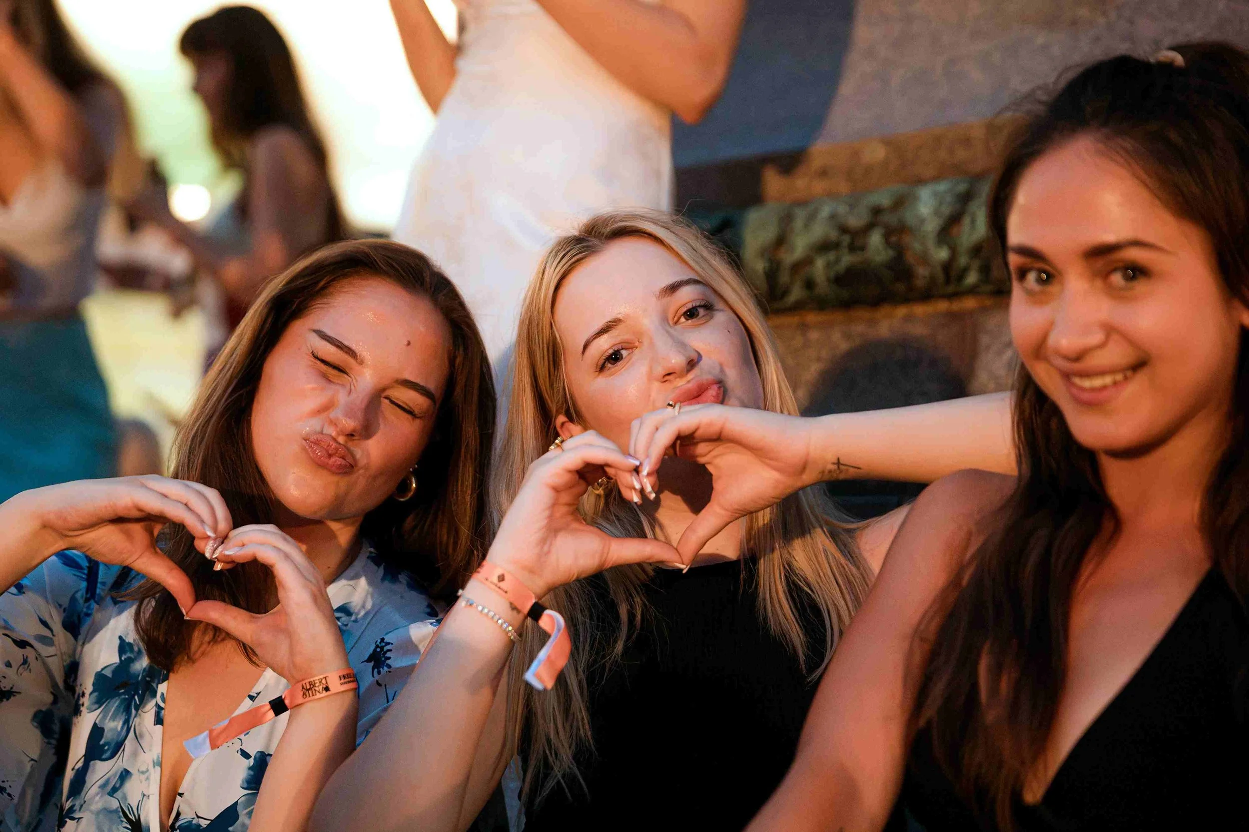 Group of young women at a social gathering making heart shapes with their hands, smiling, and posing for the photo.