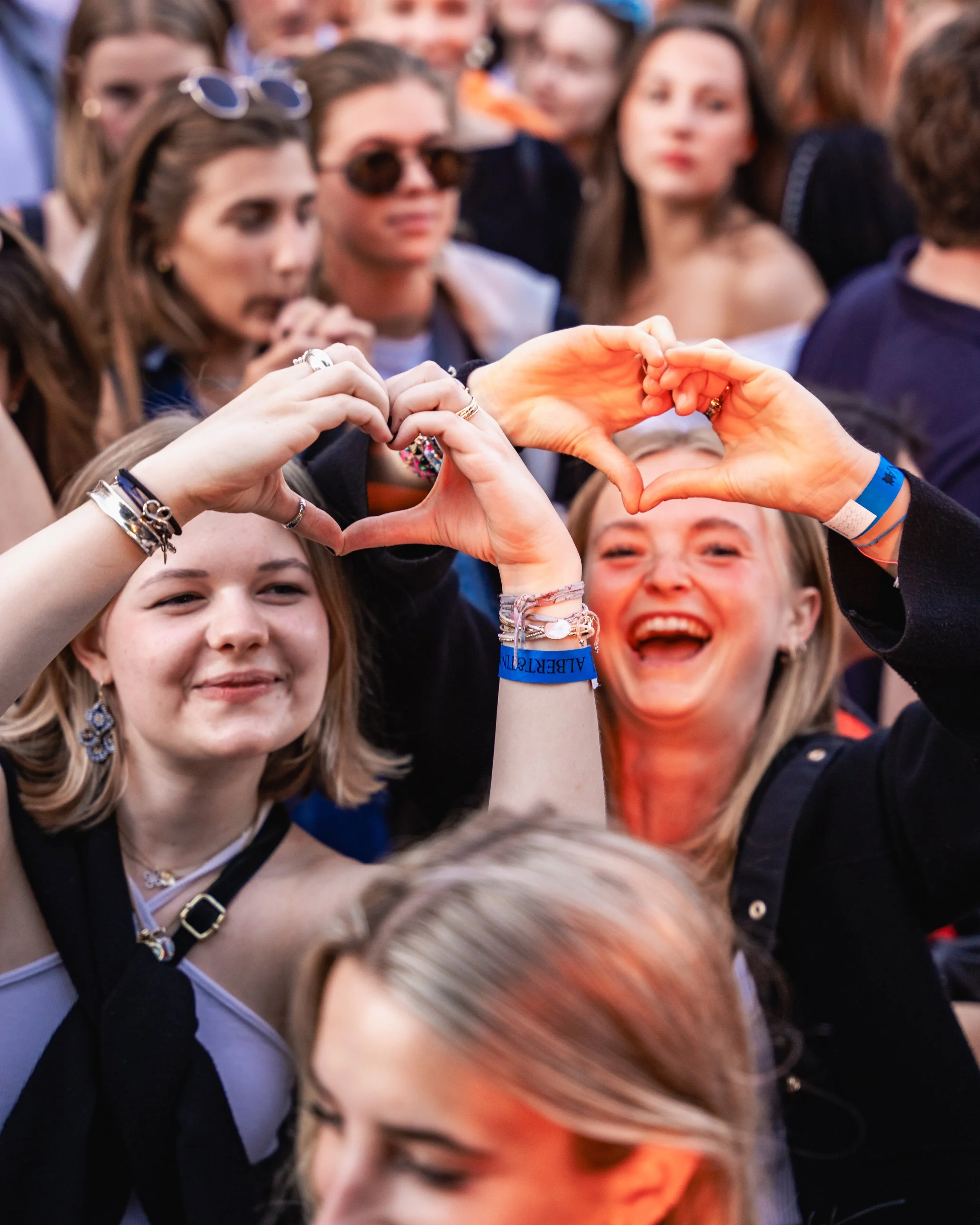 People at a crowded event making a heart shape with their hands.