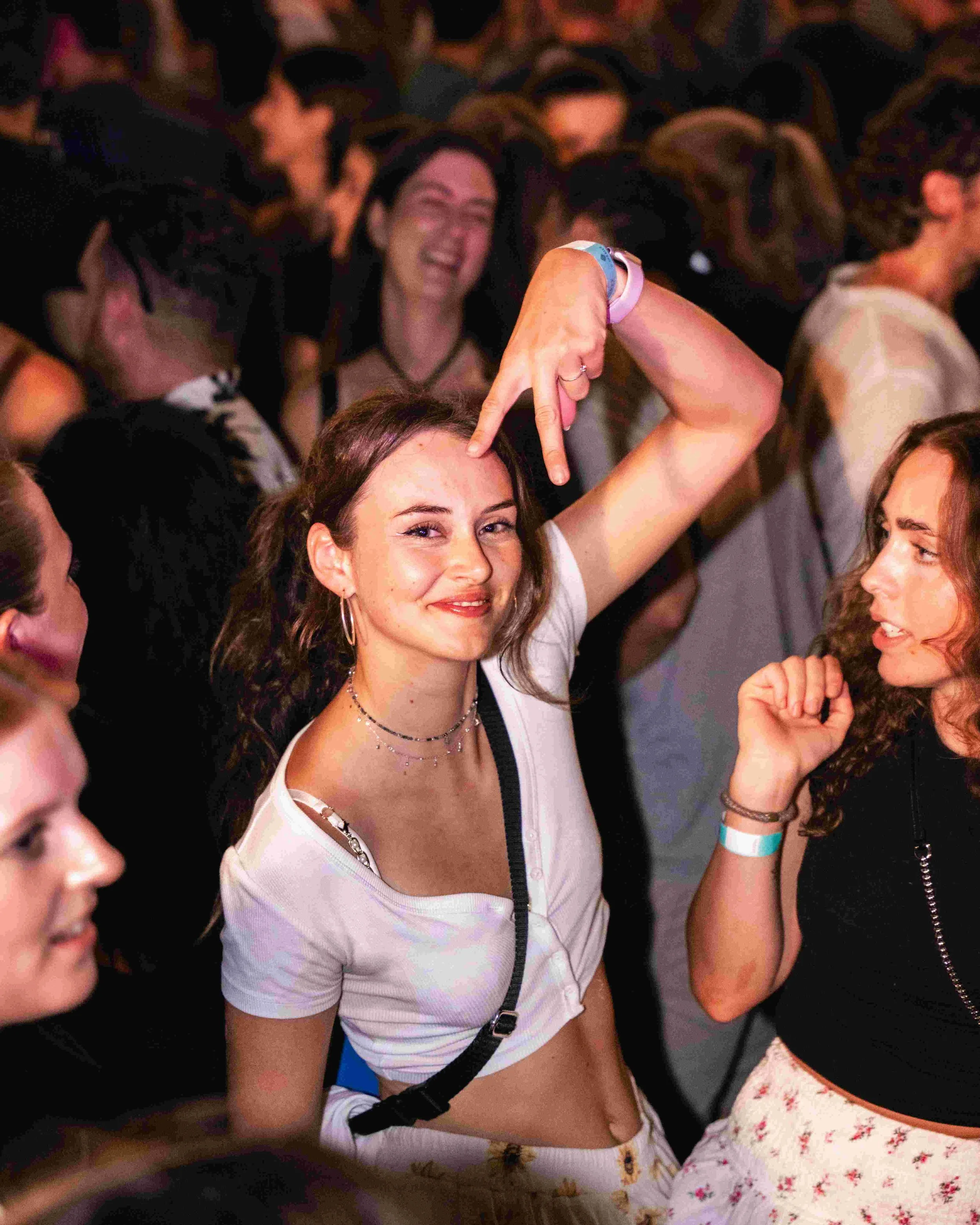 A group of young women at a party, with one woman in the center making a peace sign over her eye and smiling at the camera, surrounded by others enjoying the event.