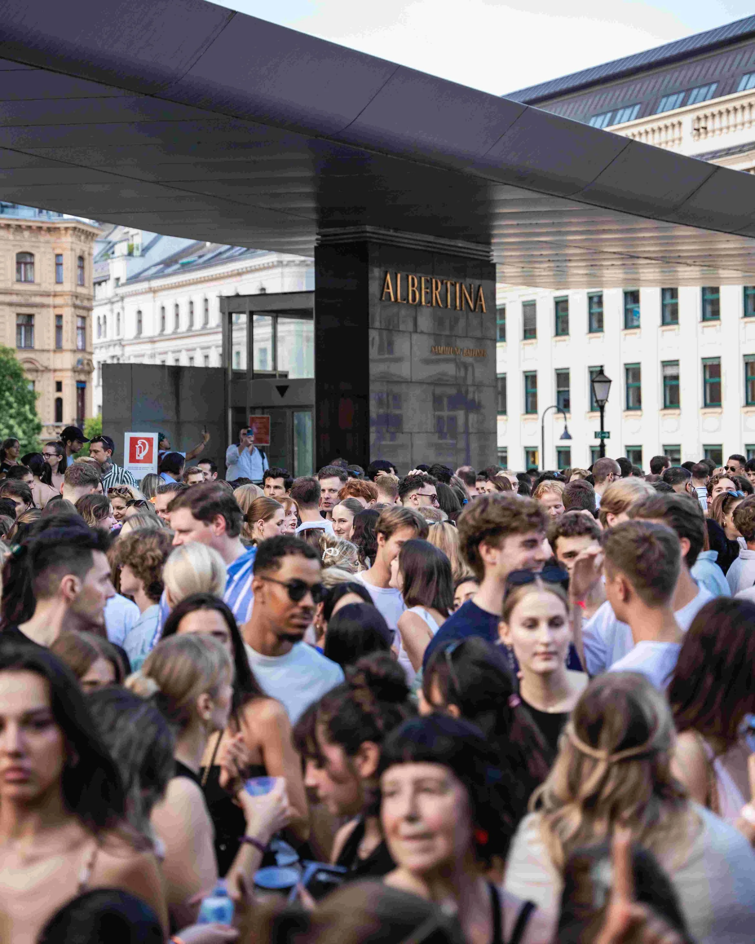 Crowd of people gathered outdoors near buildings with a sign that reads "ALBERTINA".
