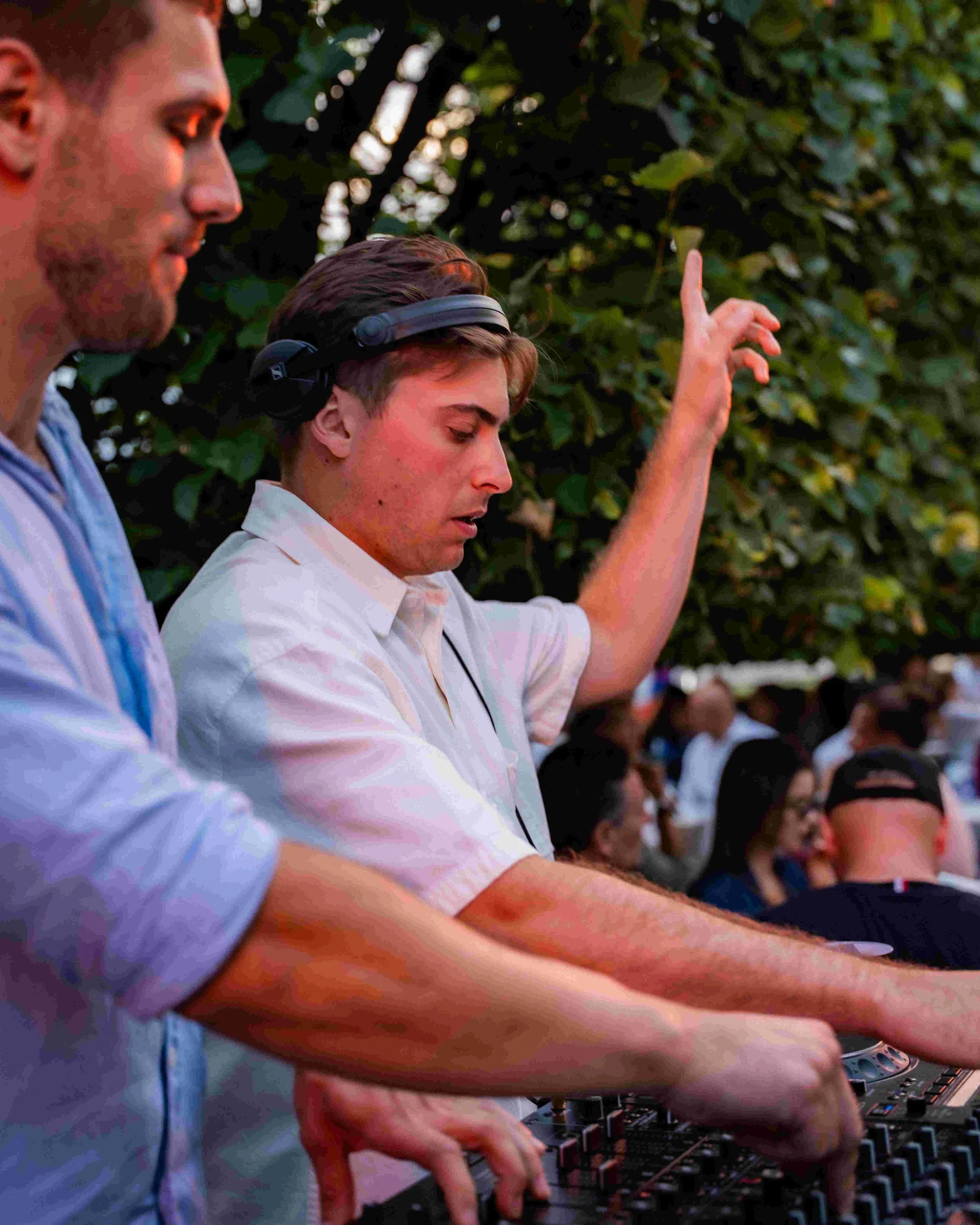 People DJing outdoors at sunset, with trees in the background.