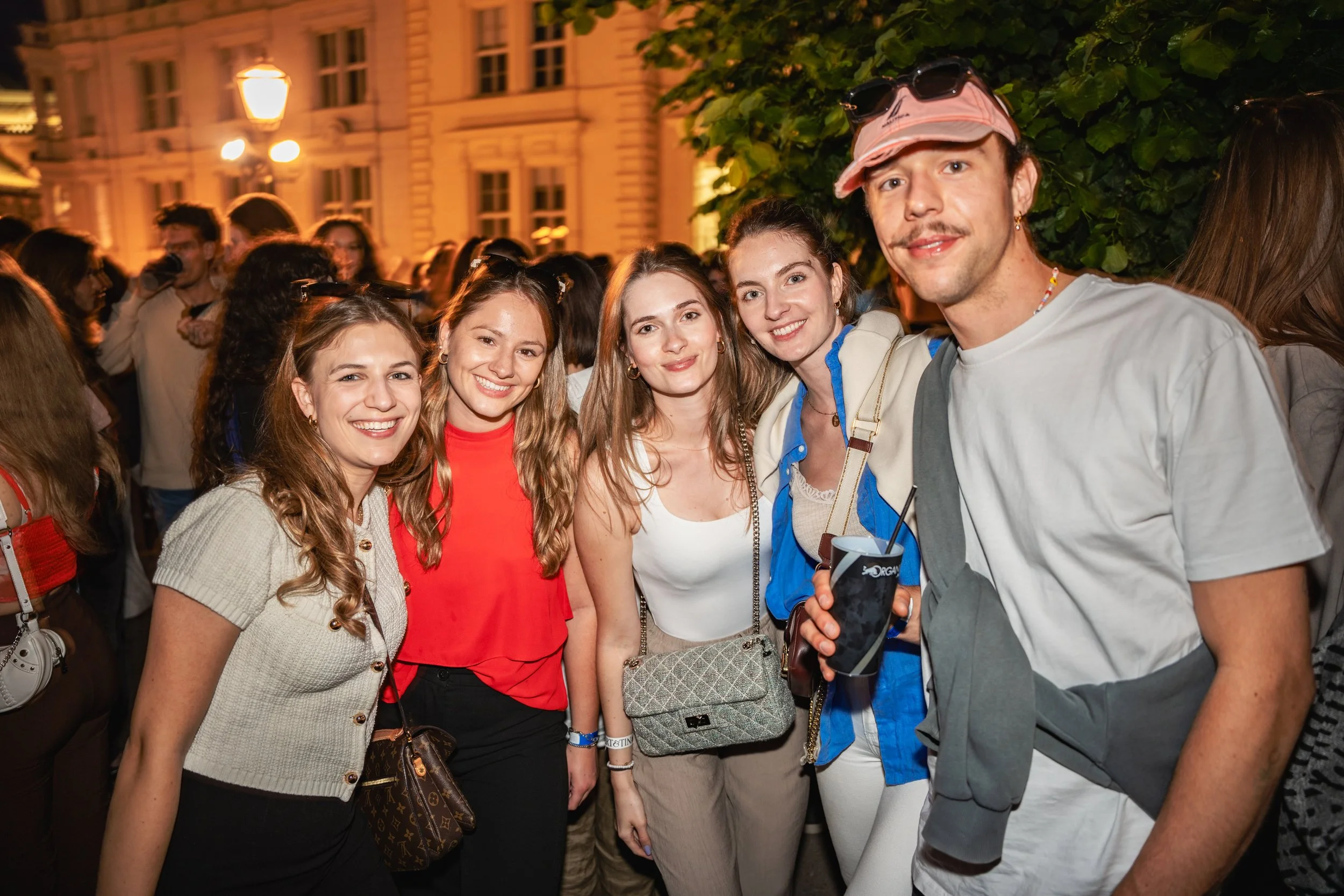 A group of young people smiling and posing together at night during a social gathering in an urban setting.