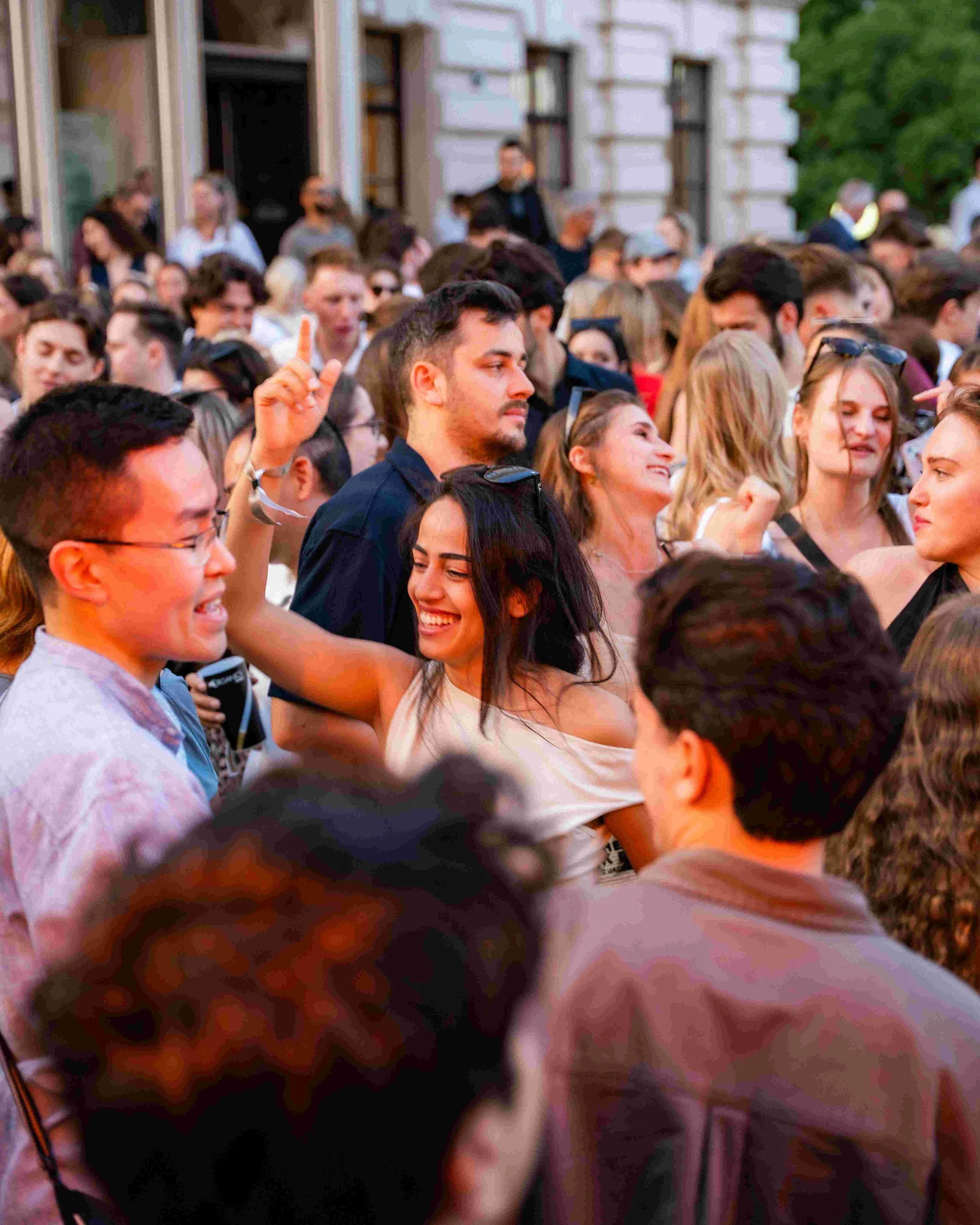 Crowd of people gathered outside near a building, some smiling and socializing.