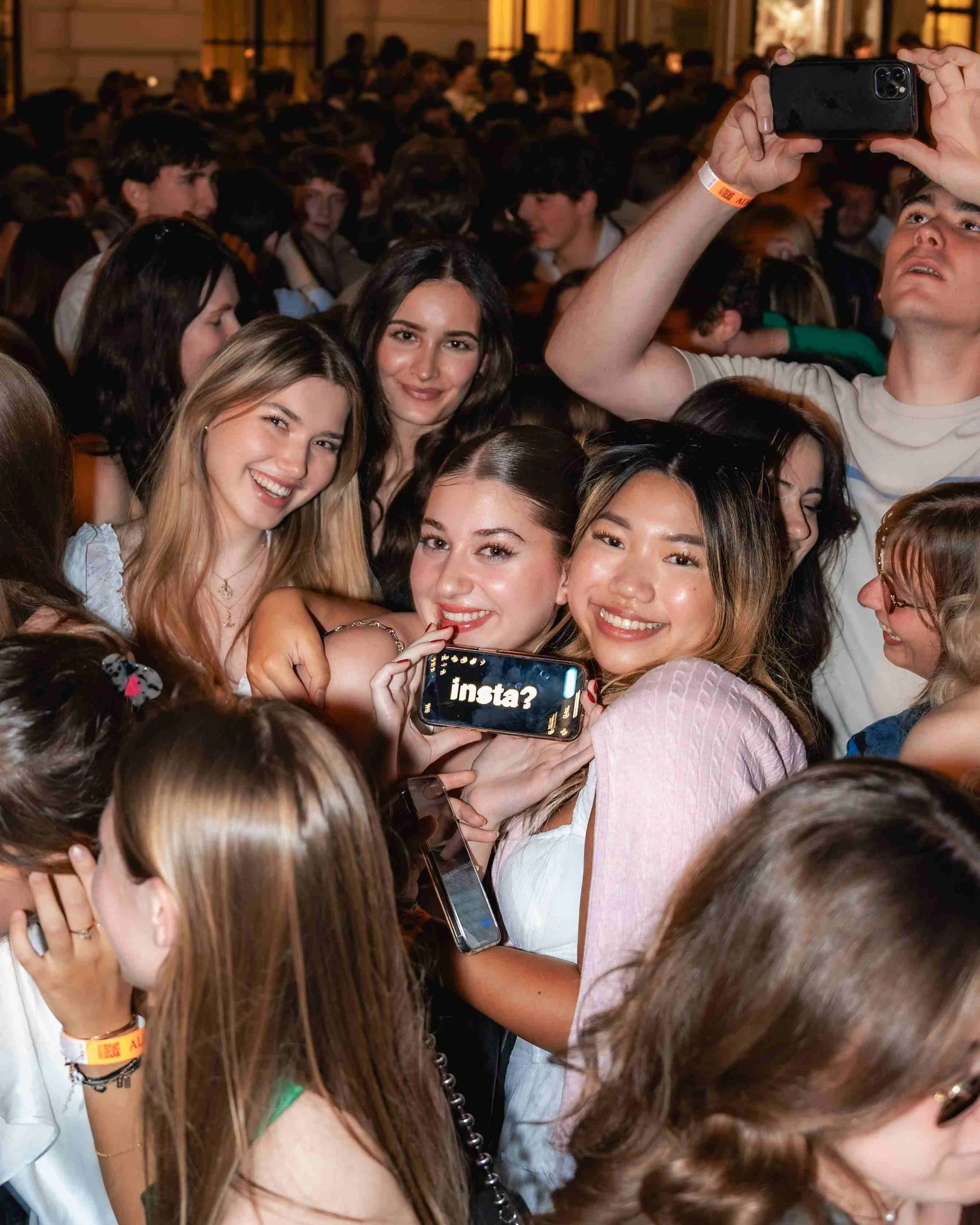 A group of young people taking a selfie at a crowded indoor event.