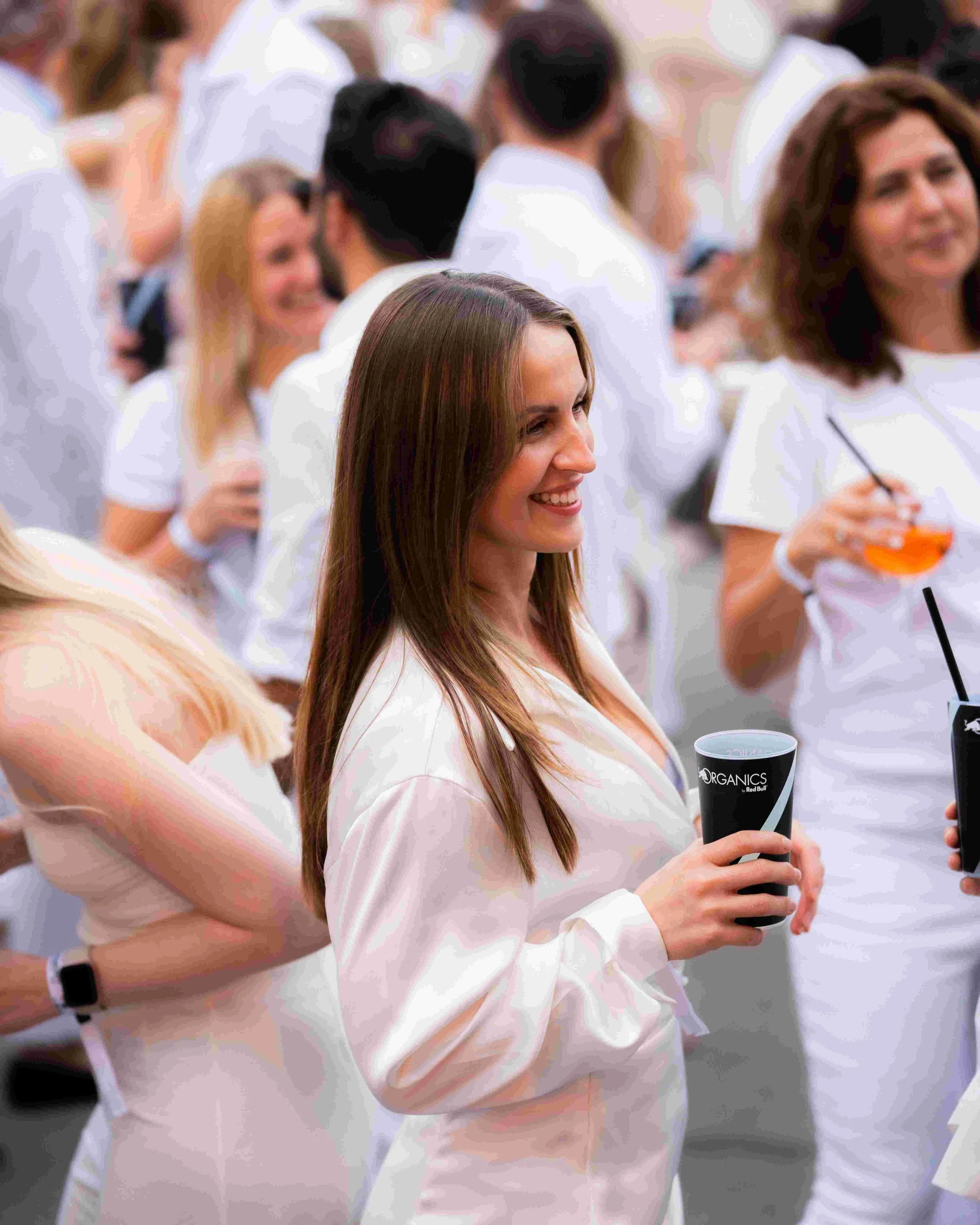A group of smiling people at an outdoor event, holding drinks, with many wearing white shirts.