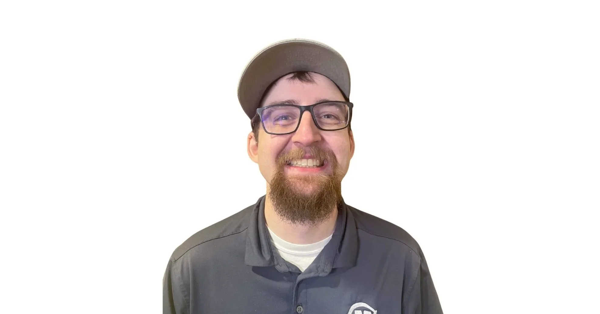 Smiling man with glasses and a beard, wearing a gray cap and dark jacket, standing against a plain white background.
