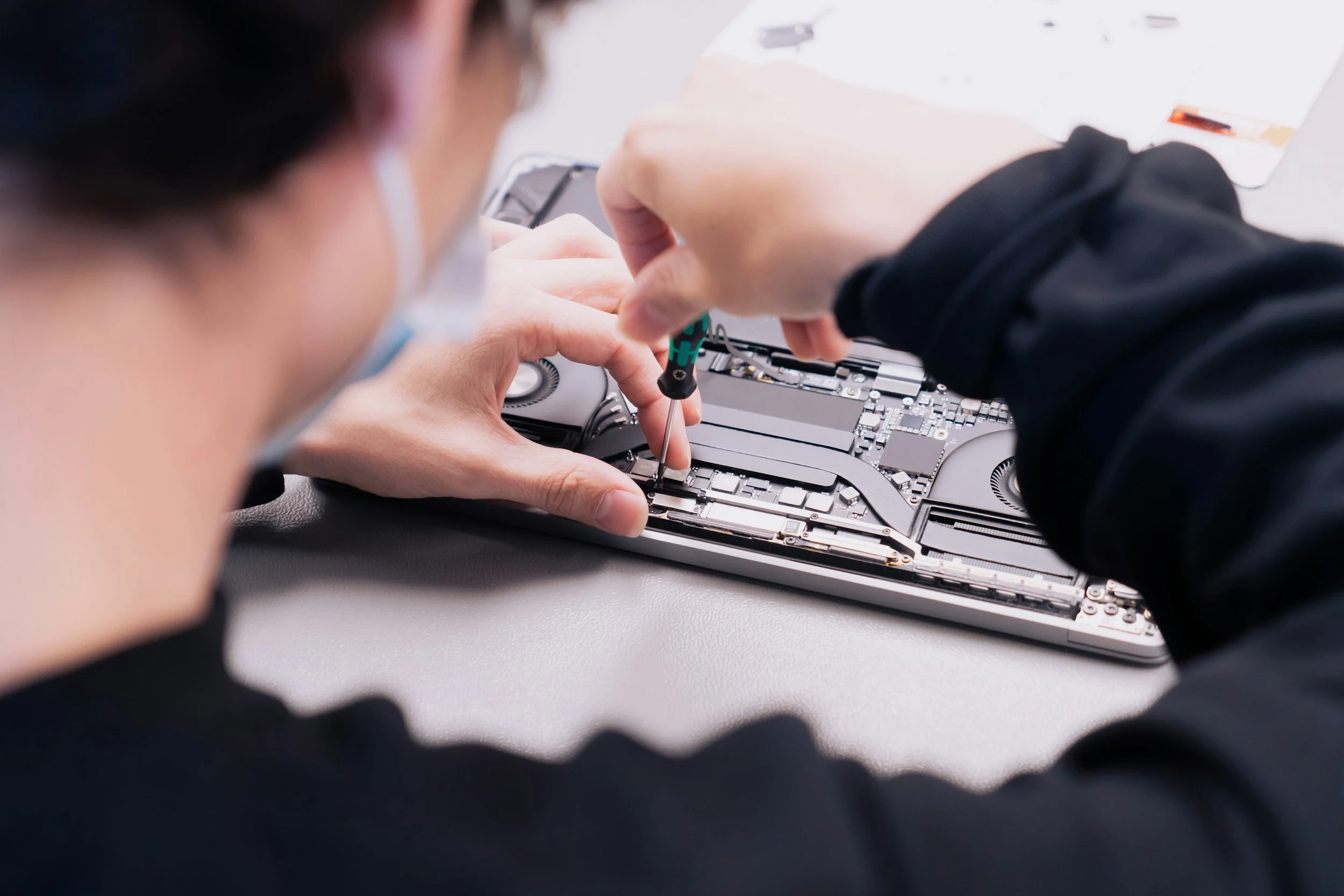 Person repairing a laptop by fixing internal components with a screwdriver.