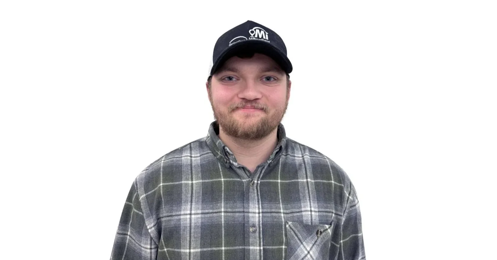 A young man with a beard, wearing a black cap and a gray plaid button-up shirt, standing against a plain white background.