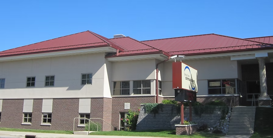 Building with red roof, white walls, and brick lower section, with a sign in front and steps leading up to the entrance.