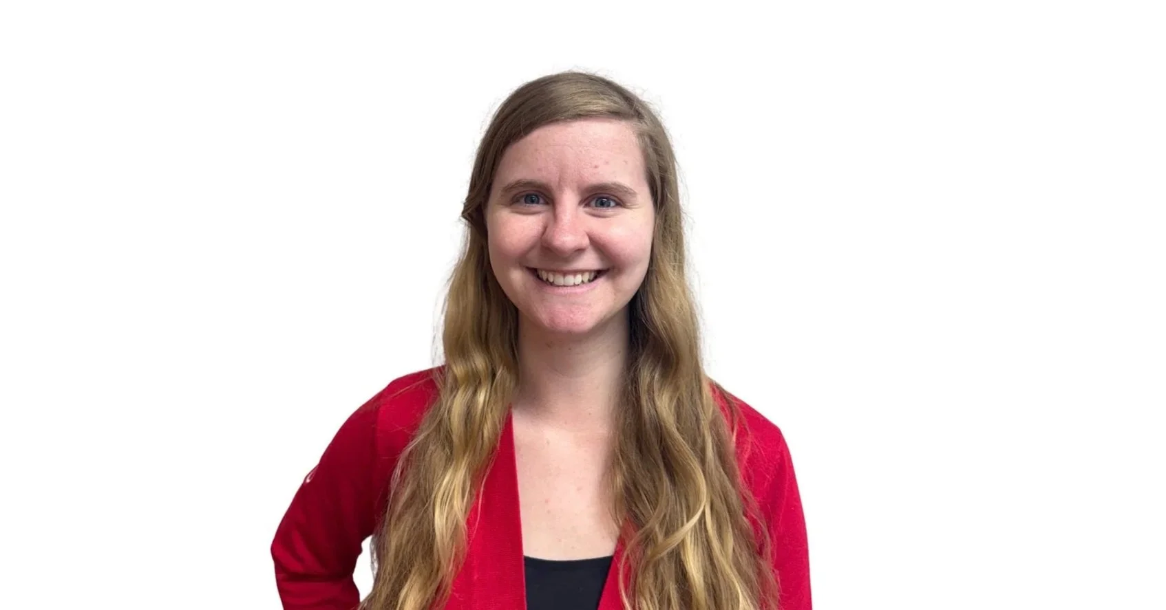 A young woman with long wavy hair, smiling, wearing a red jacket and black top, standing against a plain white background.