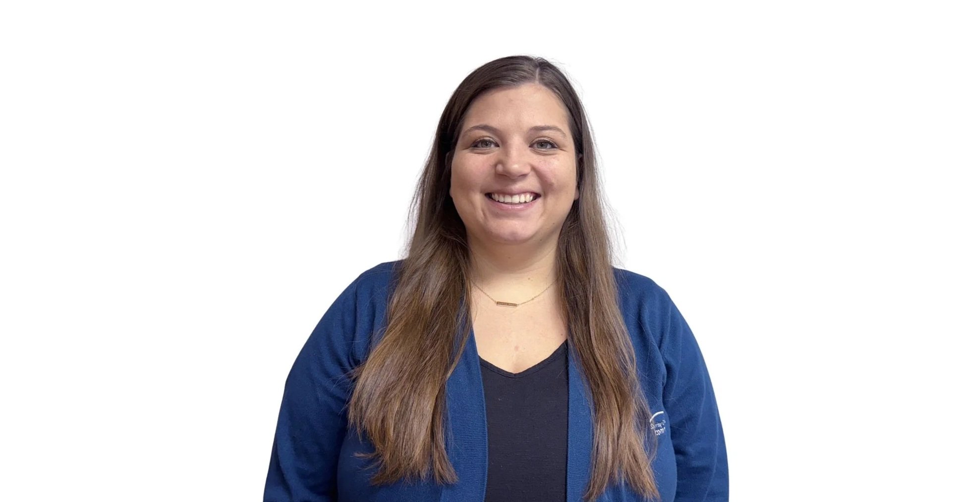 A woman with long brown hair smiling, wearing a dark shirt and a blue jacket, standing against a white background.