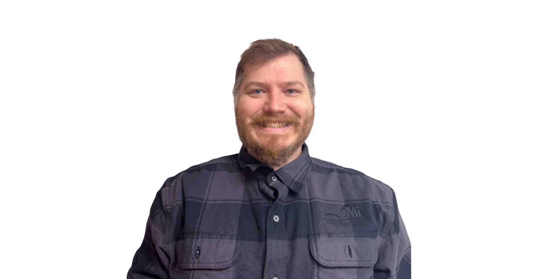 A smiling man with a beard and short hair, wearing a black and gray checkered button-up shirt, standing against a plain white background.