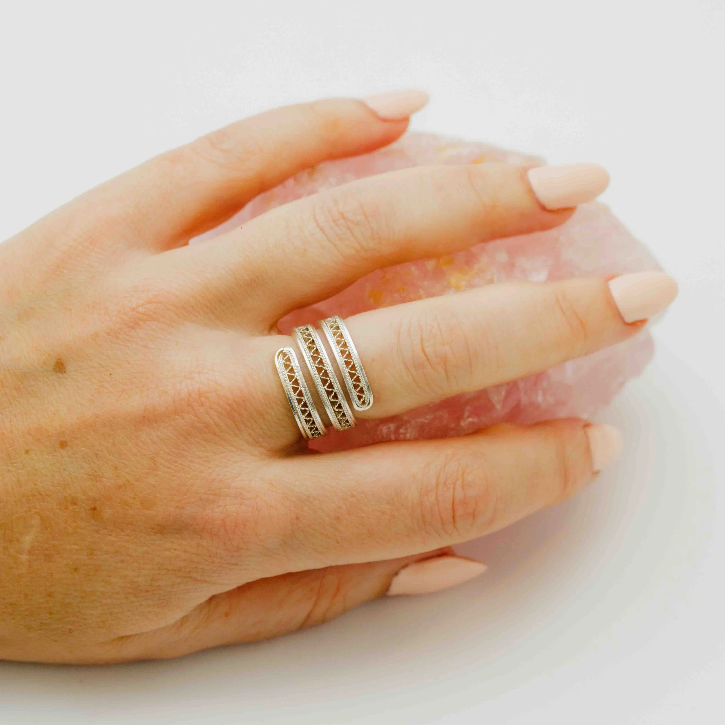 Een hand met gekleurde nagels en drie ringen. De hand rust op een zacht roze oppervlak.