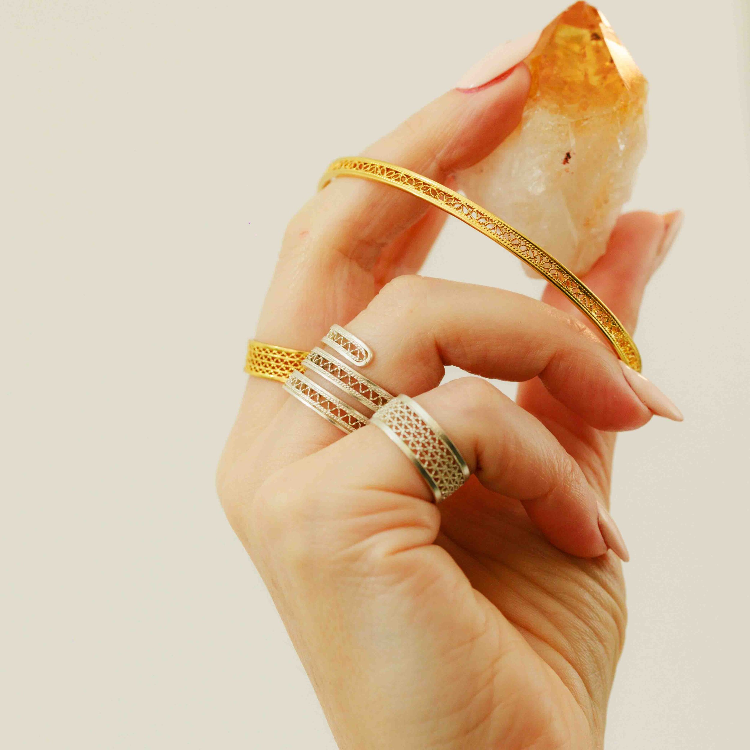 Hand met meerdere gouden en zilveren ringen, houdt een grote oranje en wit glanzende kristal of mineraal vast.
