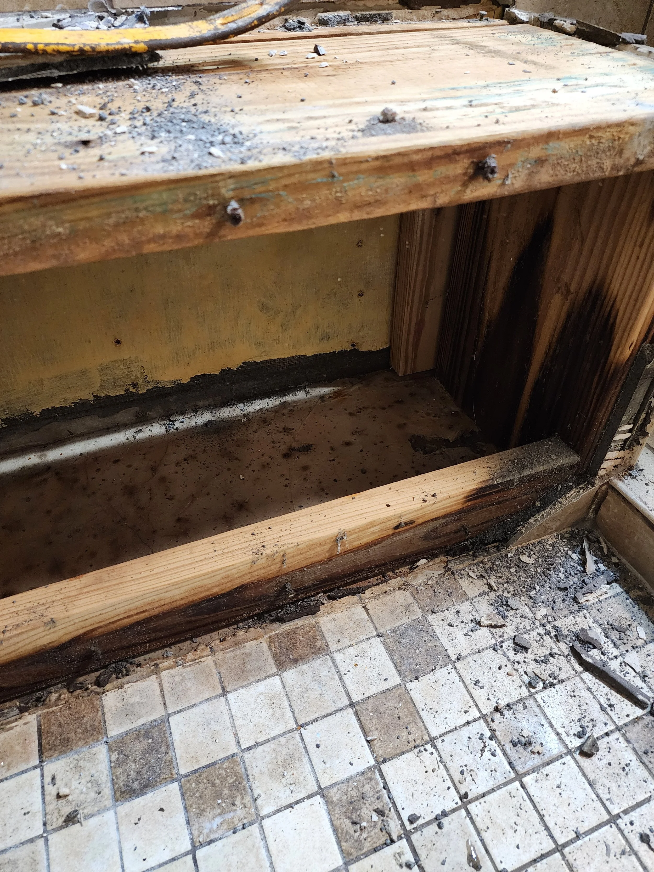 Damaged and partially removed wooden kitchen cabinet with debris on the floor and tile flooring.