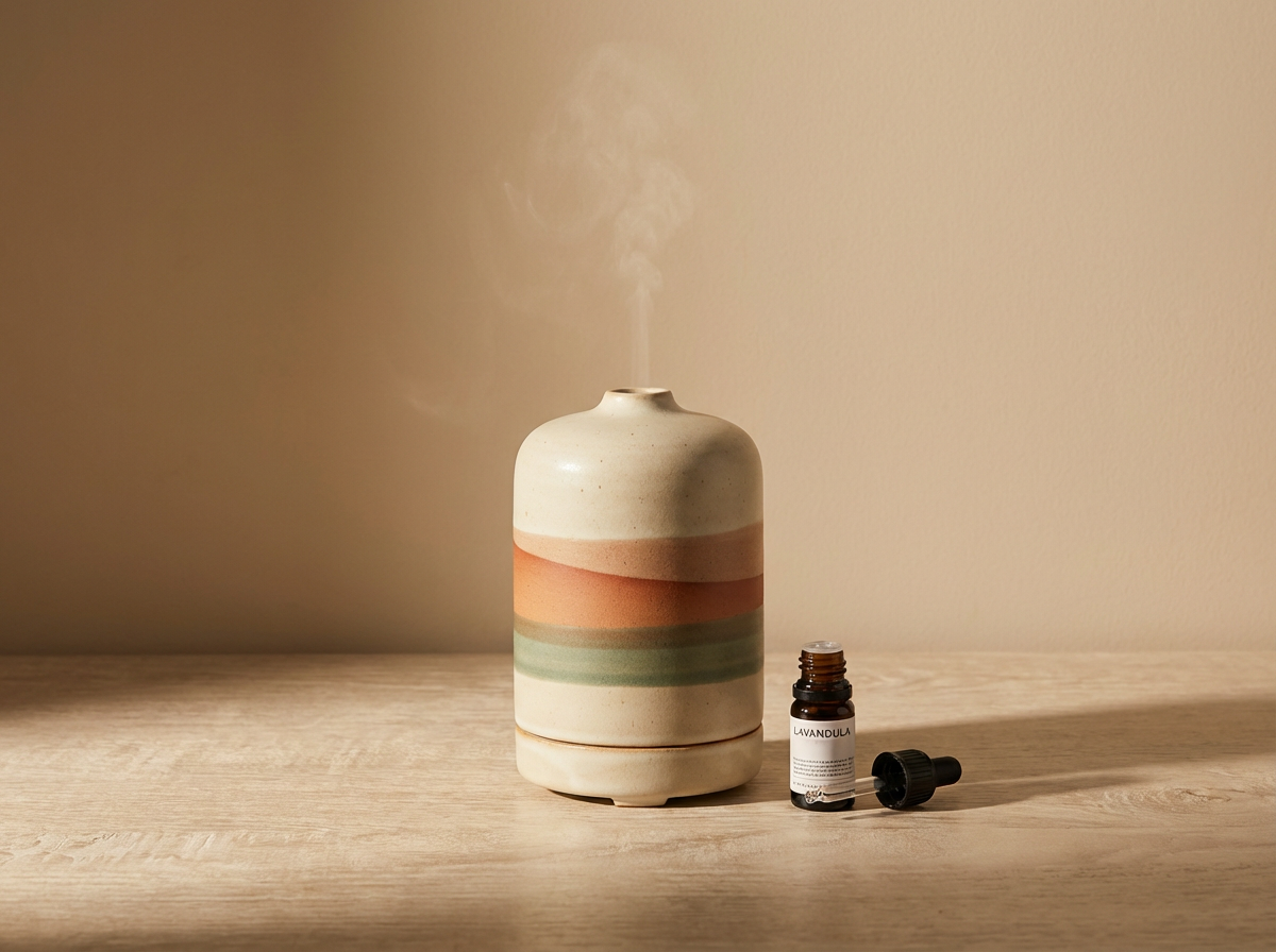 A ceramic diffuser vase with three painted horizontal stripes, emitting steam, and a small essential oil bottle labeled 'LAVANDULA' with its lid open on a wooden surface.