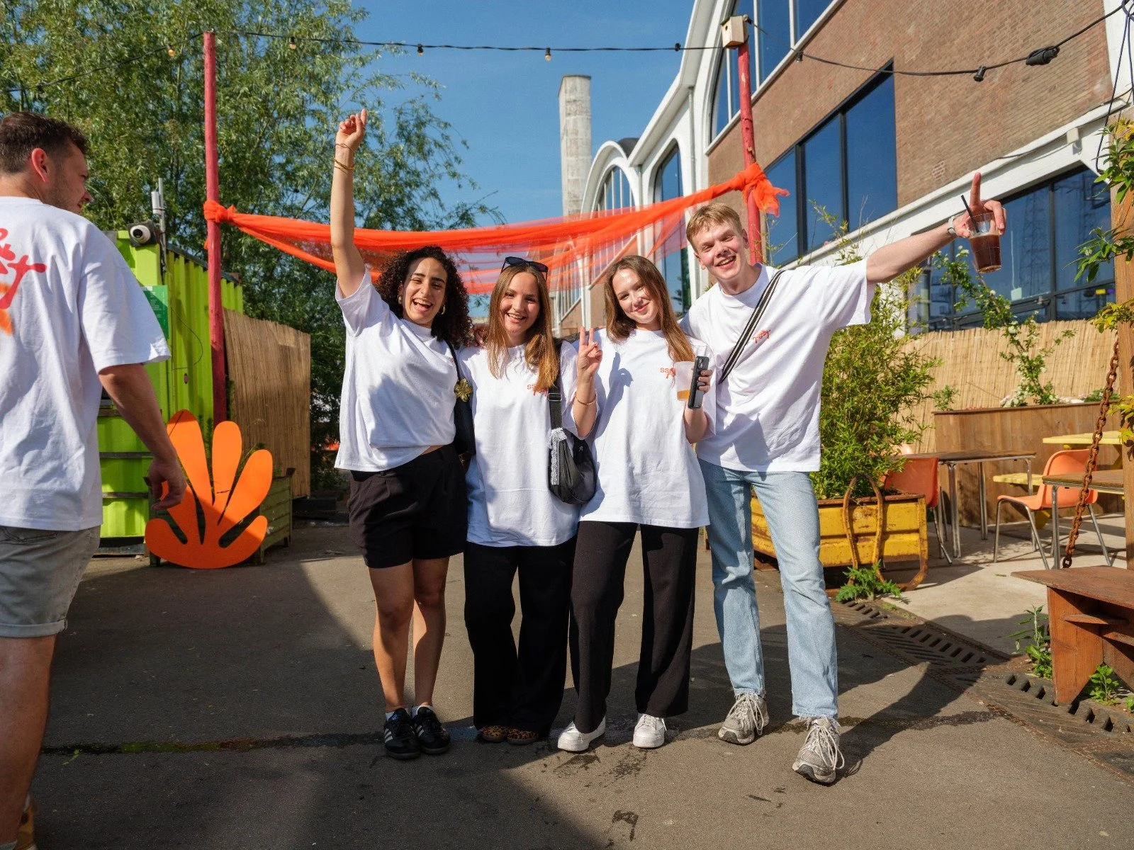 Group of five friends standing outdoors, smiling and having fun at a casual gathering, with a colorful backyard setting behind them.
